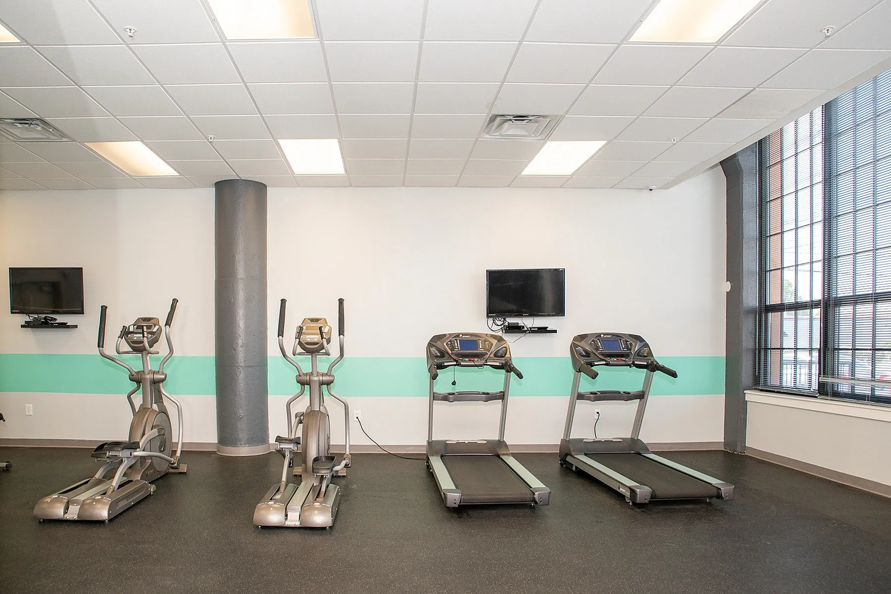 Modern fitness center with state-of-the-art treadmills and ellipticals, bright interior, and large windows for natural light.
