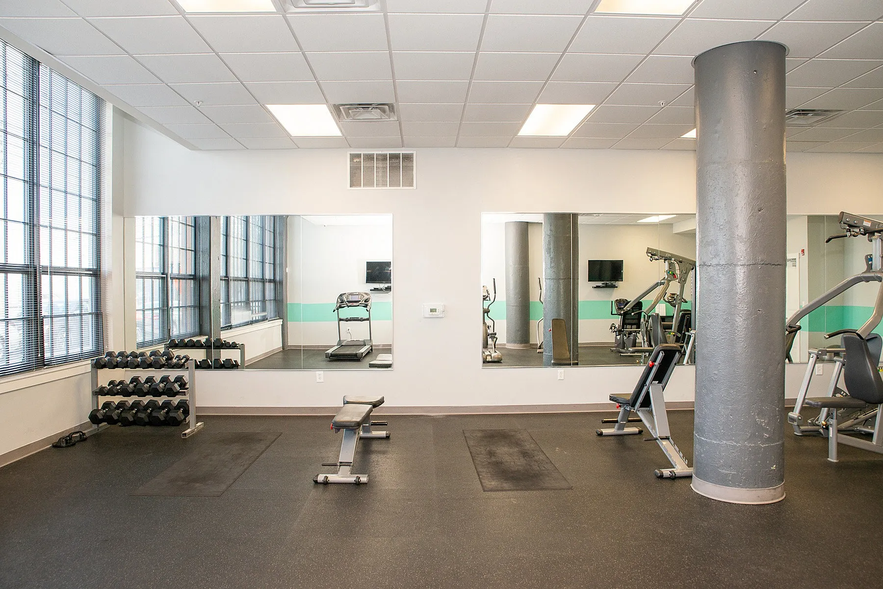 Modern fitness center with floor-to-ceiling windows, featuring free weights, a treadmill, and exercise equipment in a spacious, well-lit environment.