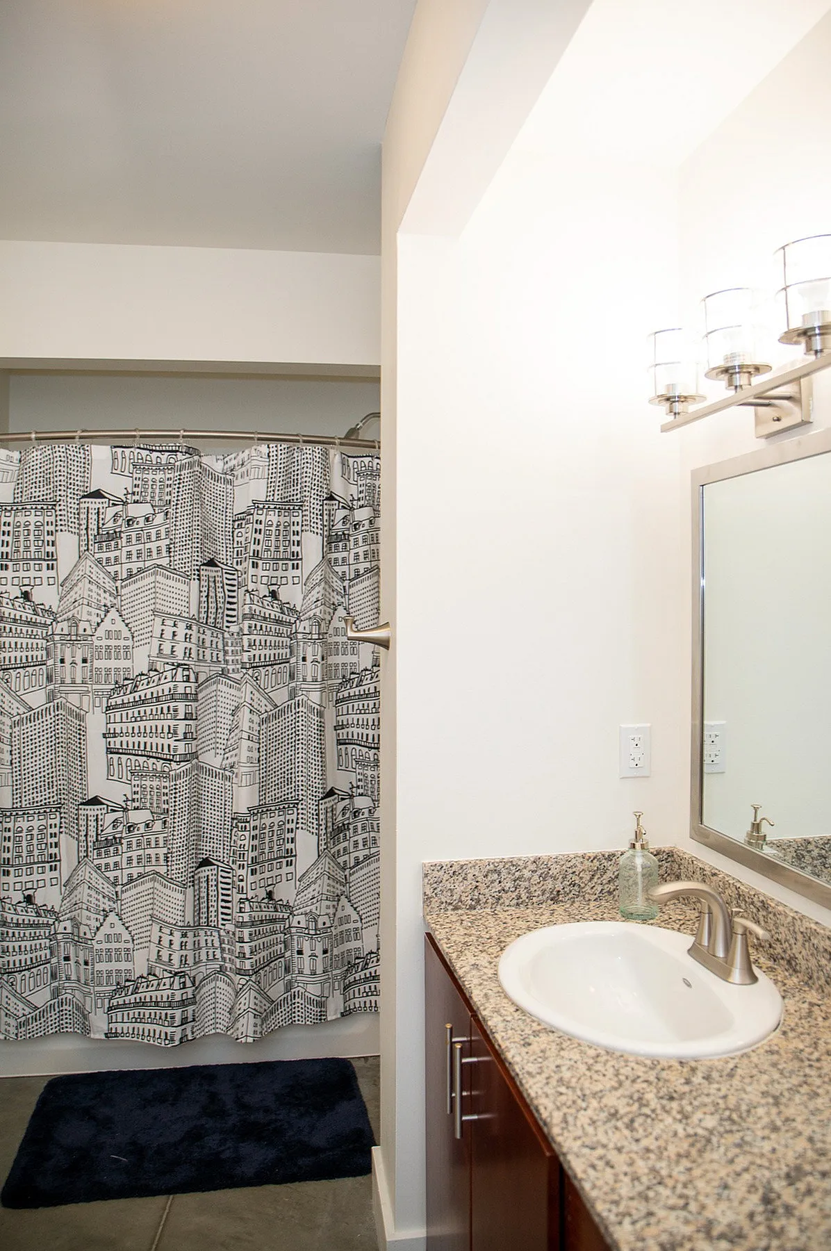 Modern bathroom featuring elegant granite countertops, stylish vanity mirror, and a chic cityscape shower curtain.