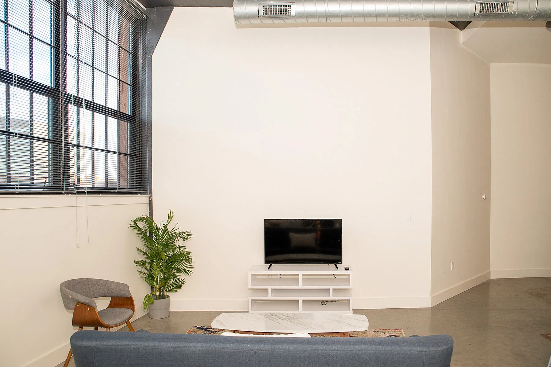 Modern living room with large industrial windows, sleek TV setup, and contemporary furniture.