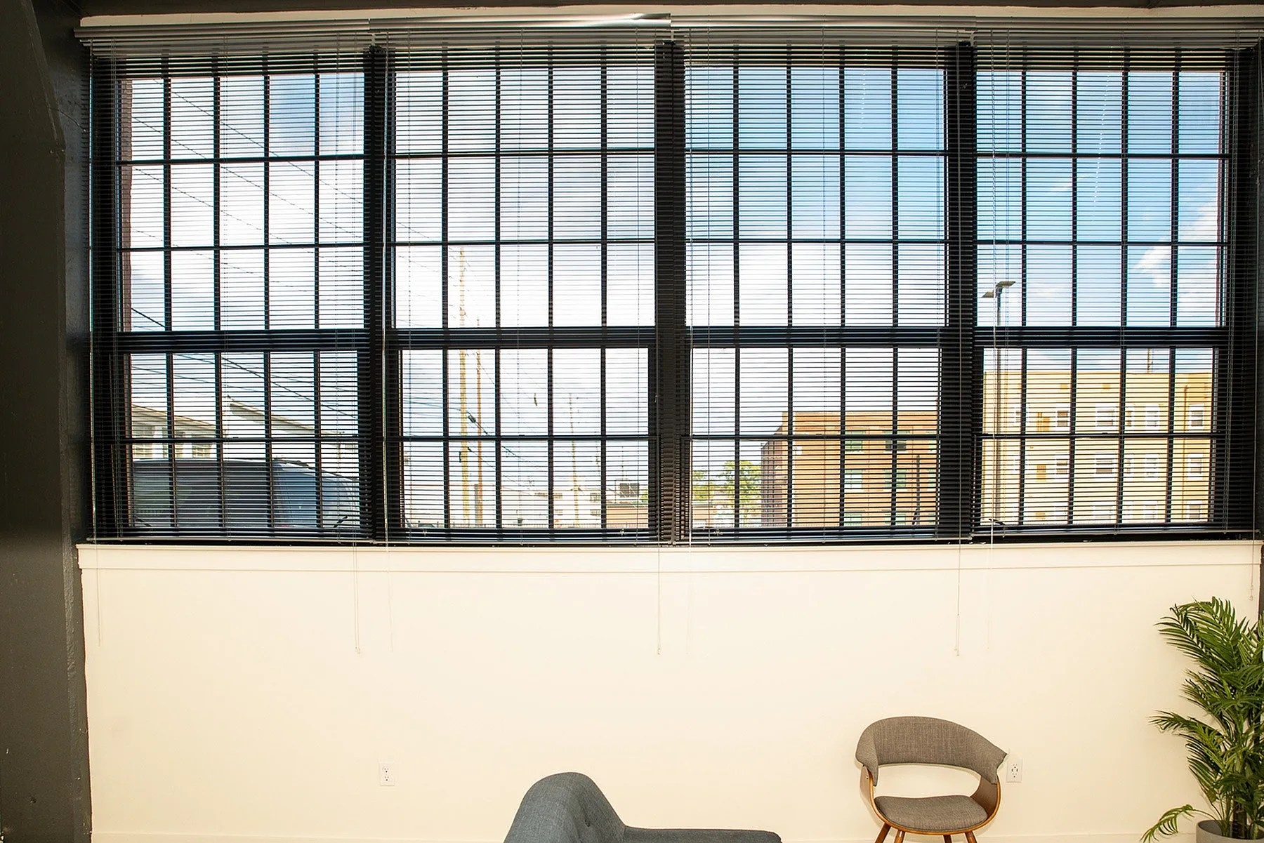 Bright apartment window with modern blinds offering a stunning city view, complemented by stylish furniture and a touch of greenery.