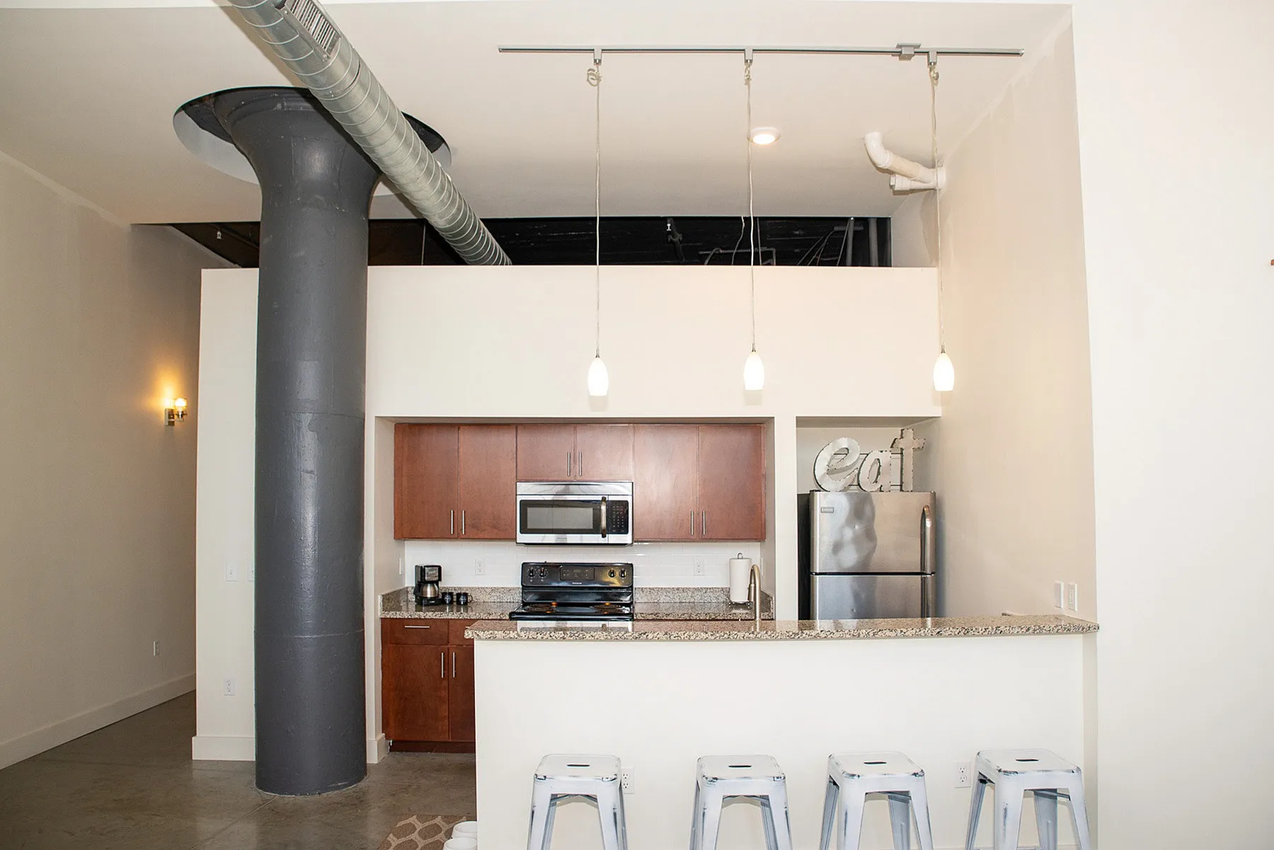 Chic industrial-style kitchen with high ceilings, featuring modern appliances, a granite countertop, and sleek pendant lighting.