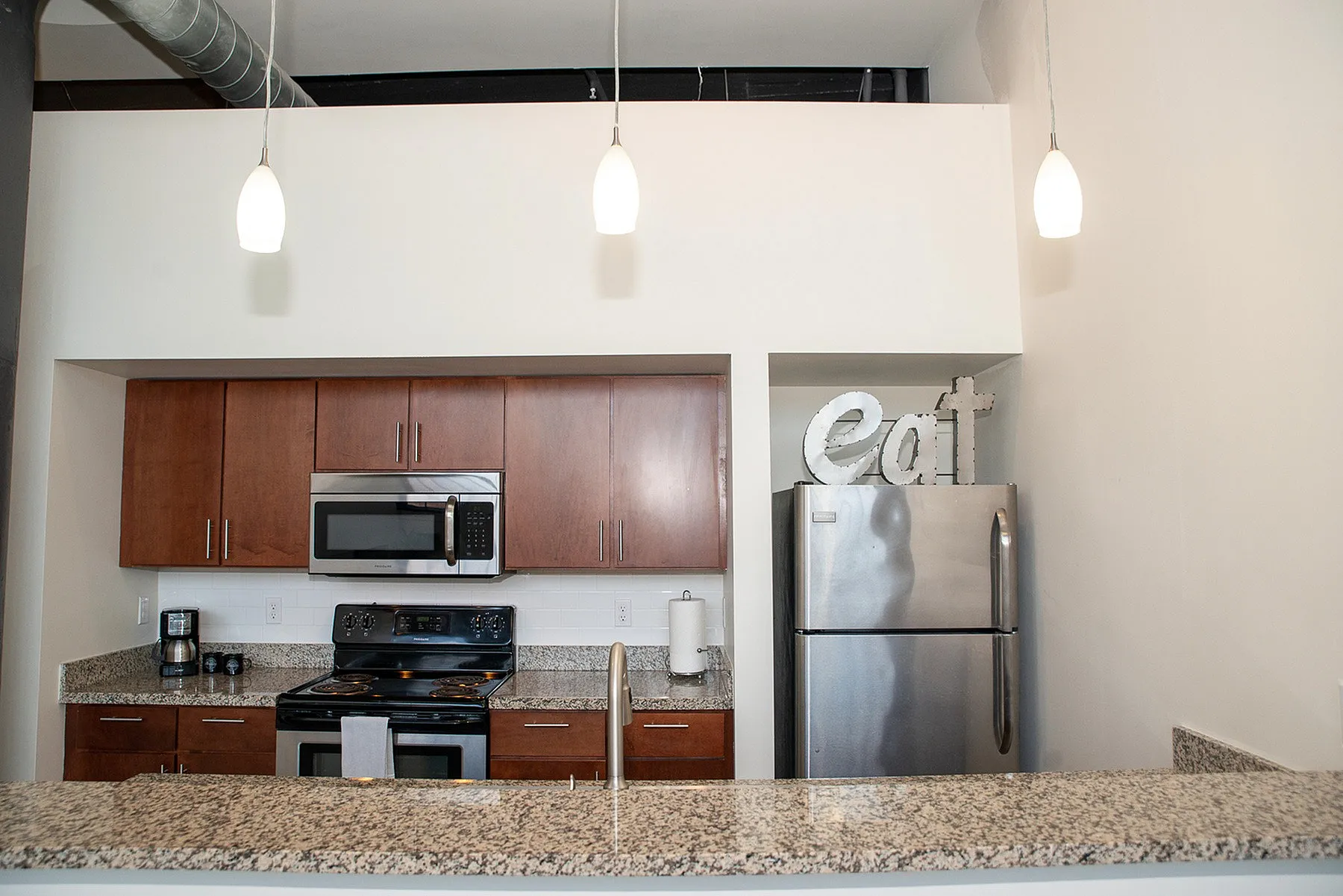 Contemporary kitchen with granite countertops, stainless steel appliances, and warm wooden cabinetry, accentuated by modern pendant lighting.