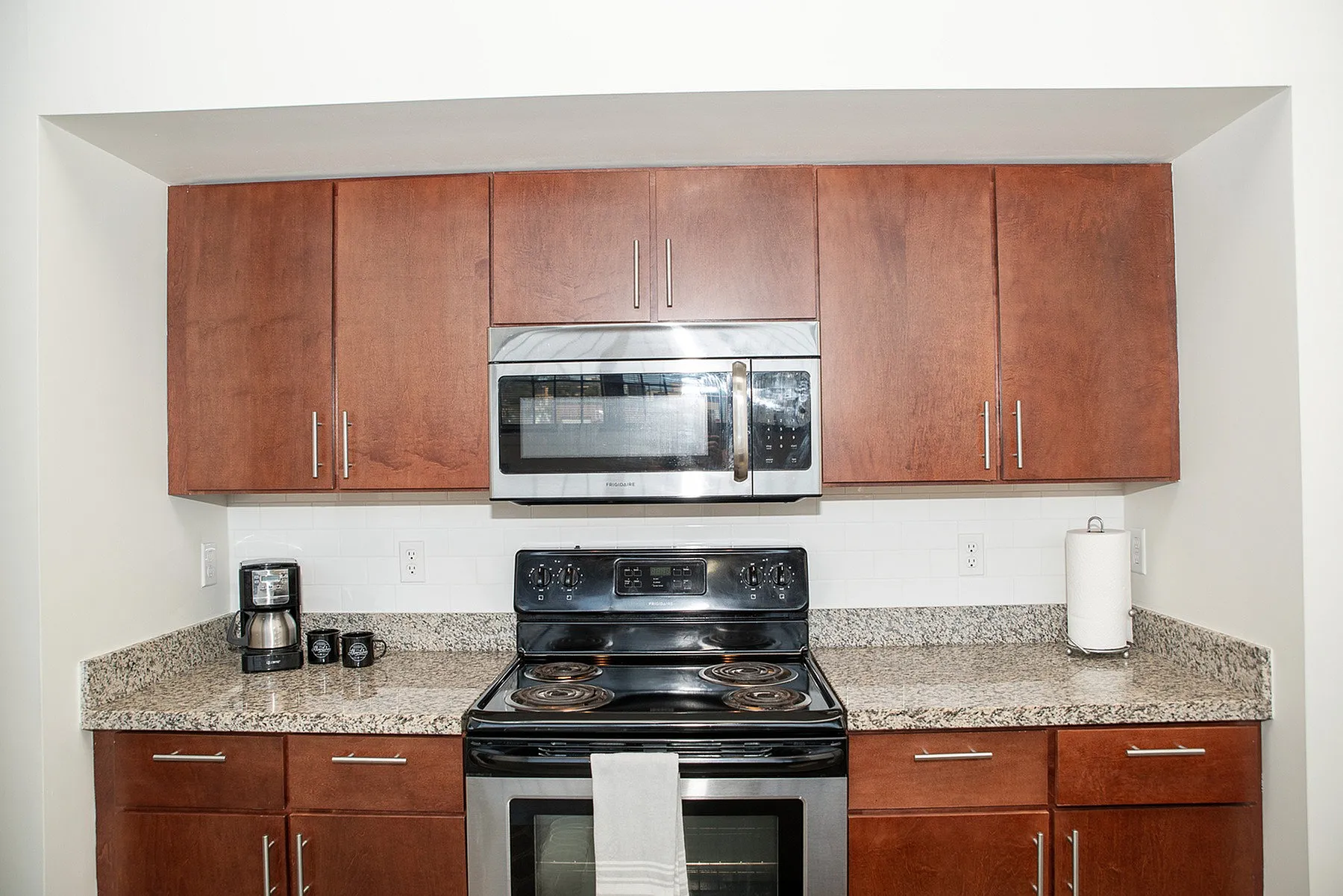 Elegant kitchen with rich wooden cabinets, sleek microwave, and modern stove, set against a stylish granite countertop.
