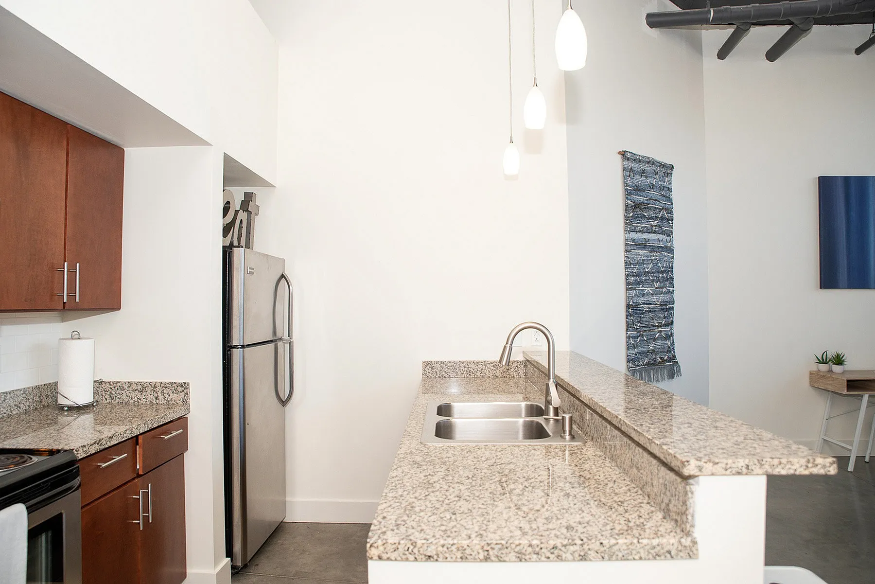 Modern kitchen with sleek granite countertops, stainless steel appliances, and elegant pendant lighting, creating a stylish space.