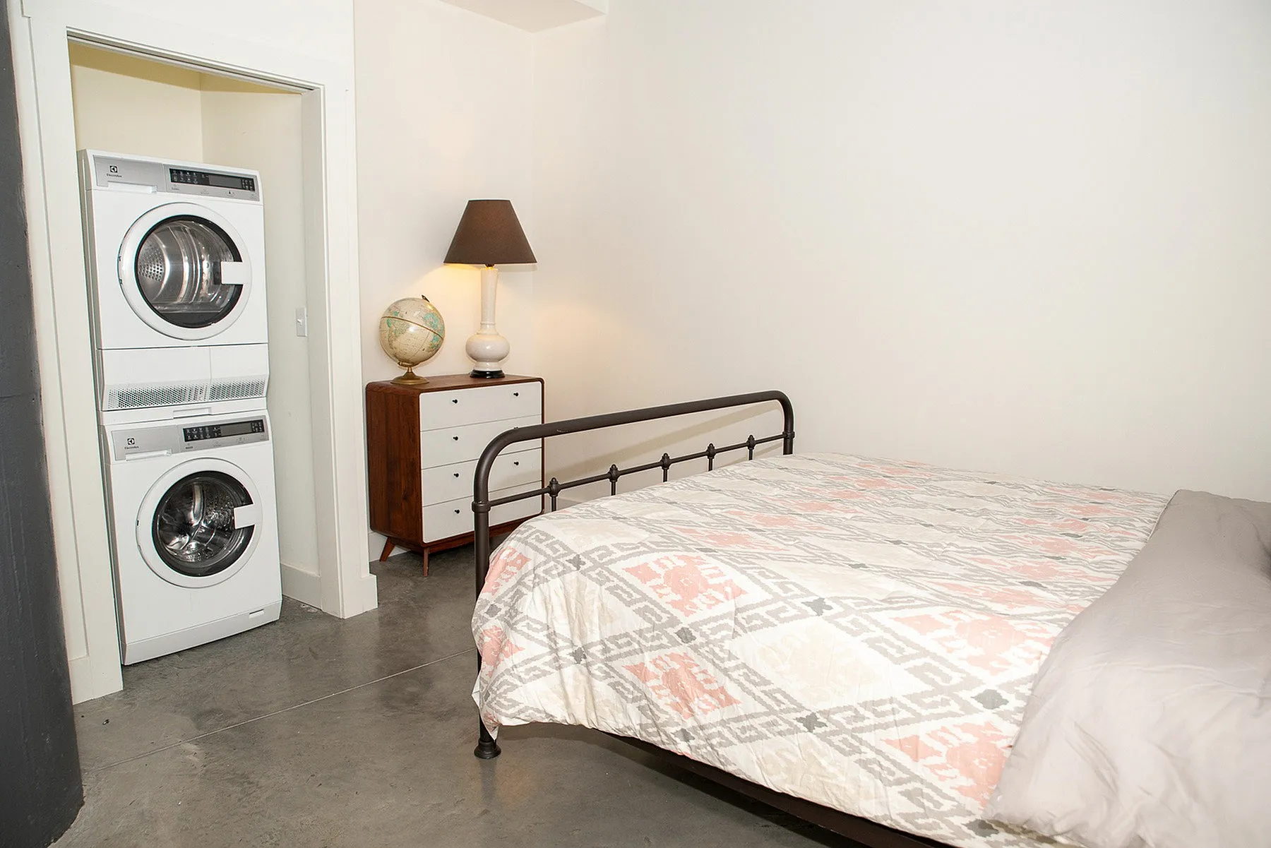 Inviting bedroom with modern stacked washer and dryer, stylish iron bed frame, and elegant decor.