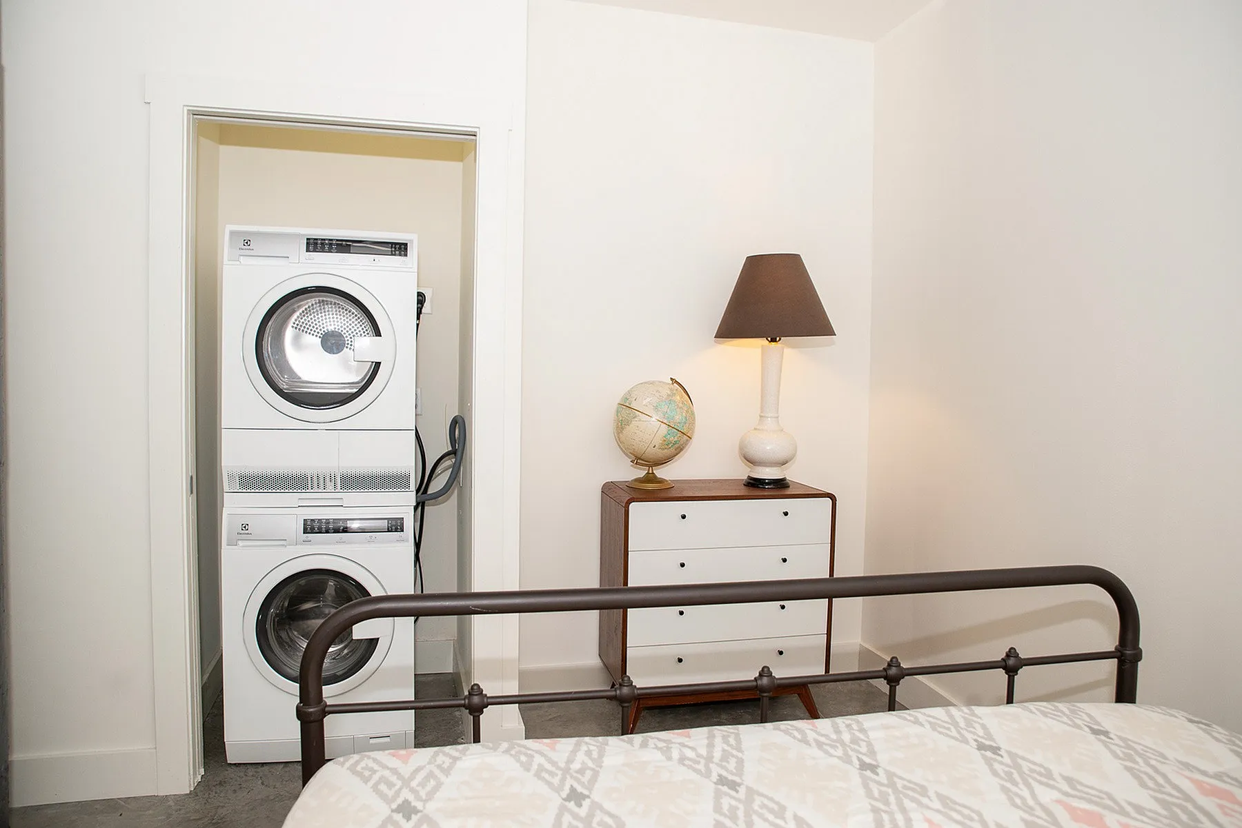 Cozy bedroom with an in-unit stacked washer and dryer, chic dresser with globe and lamp.