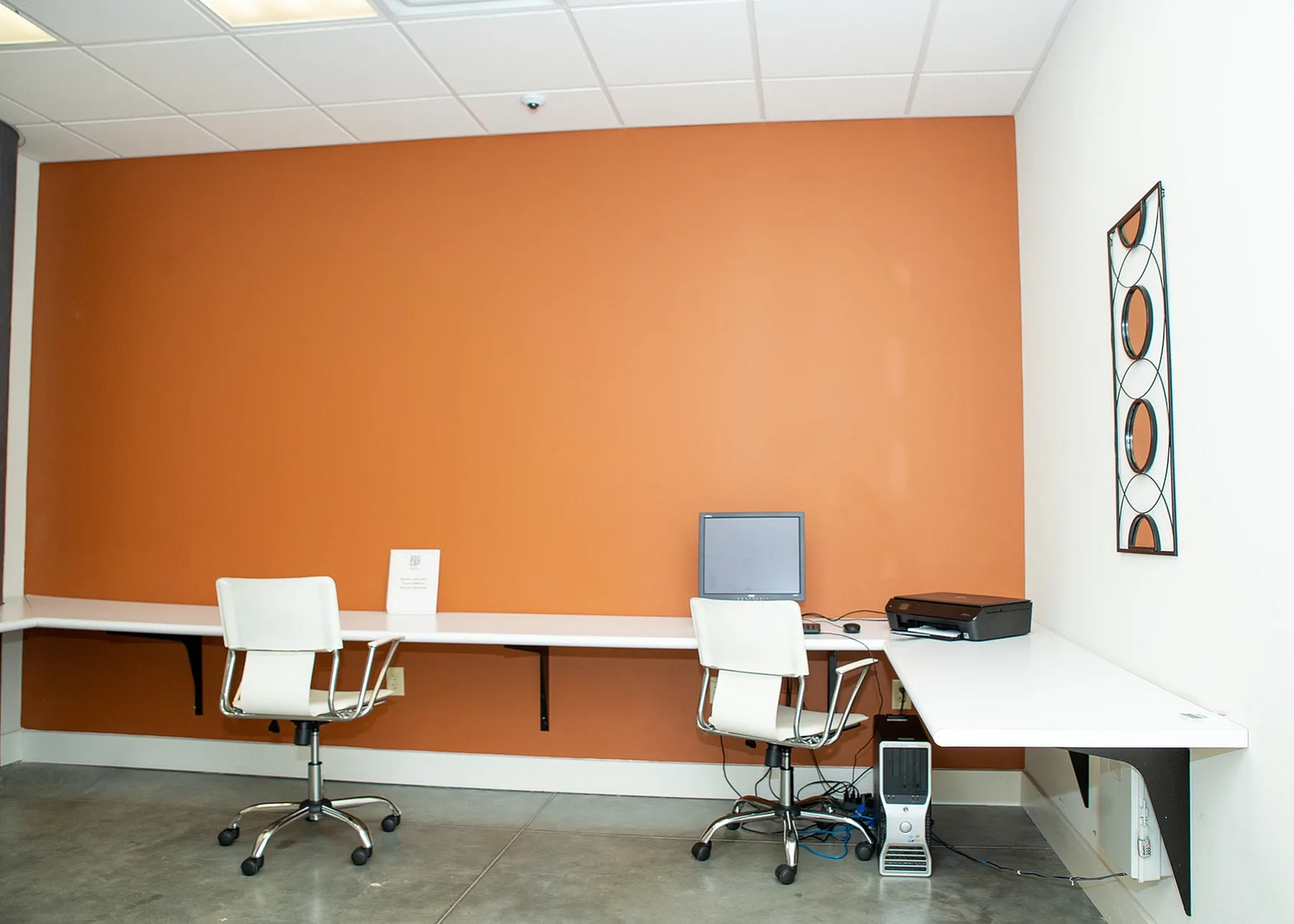 Modern office space with vibrant orange accent wall, equipped with two white chairs, sleek desk, and a computer station.