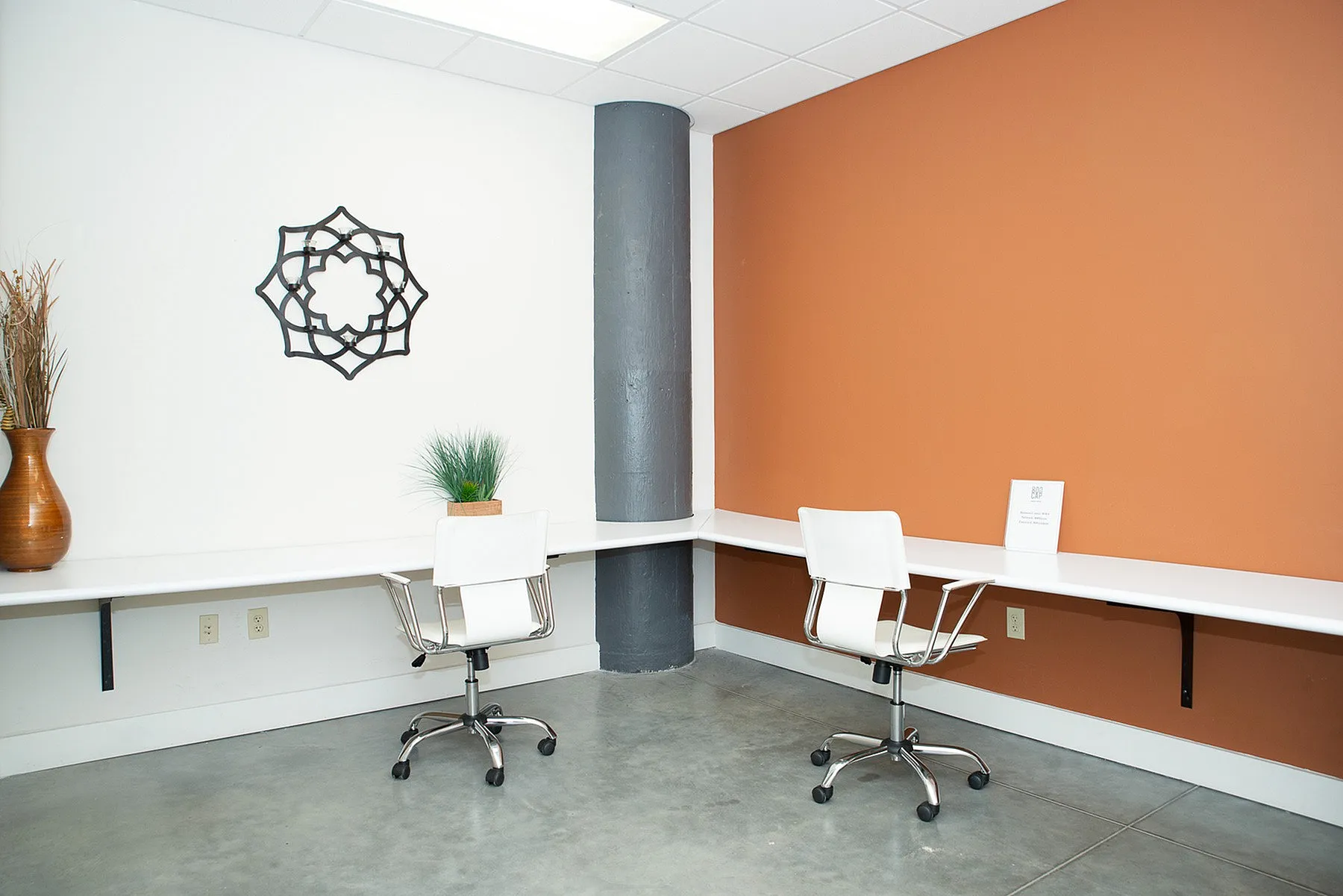 Modern office space with elegant white desks, stylish chairs, and warm orange accent wall.