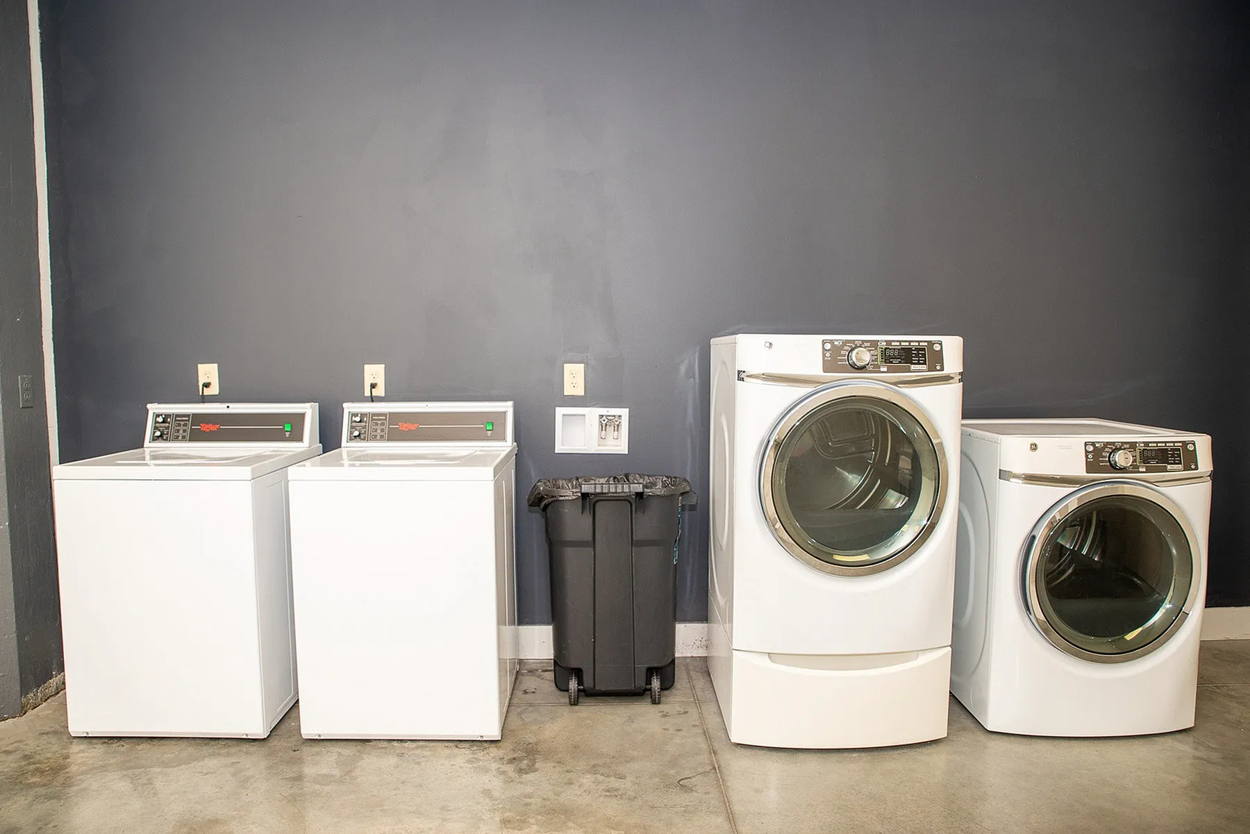 Modern laundry room with two sleek washers and dryers against a stylish gray wall.