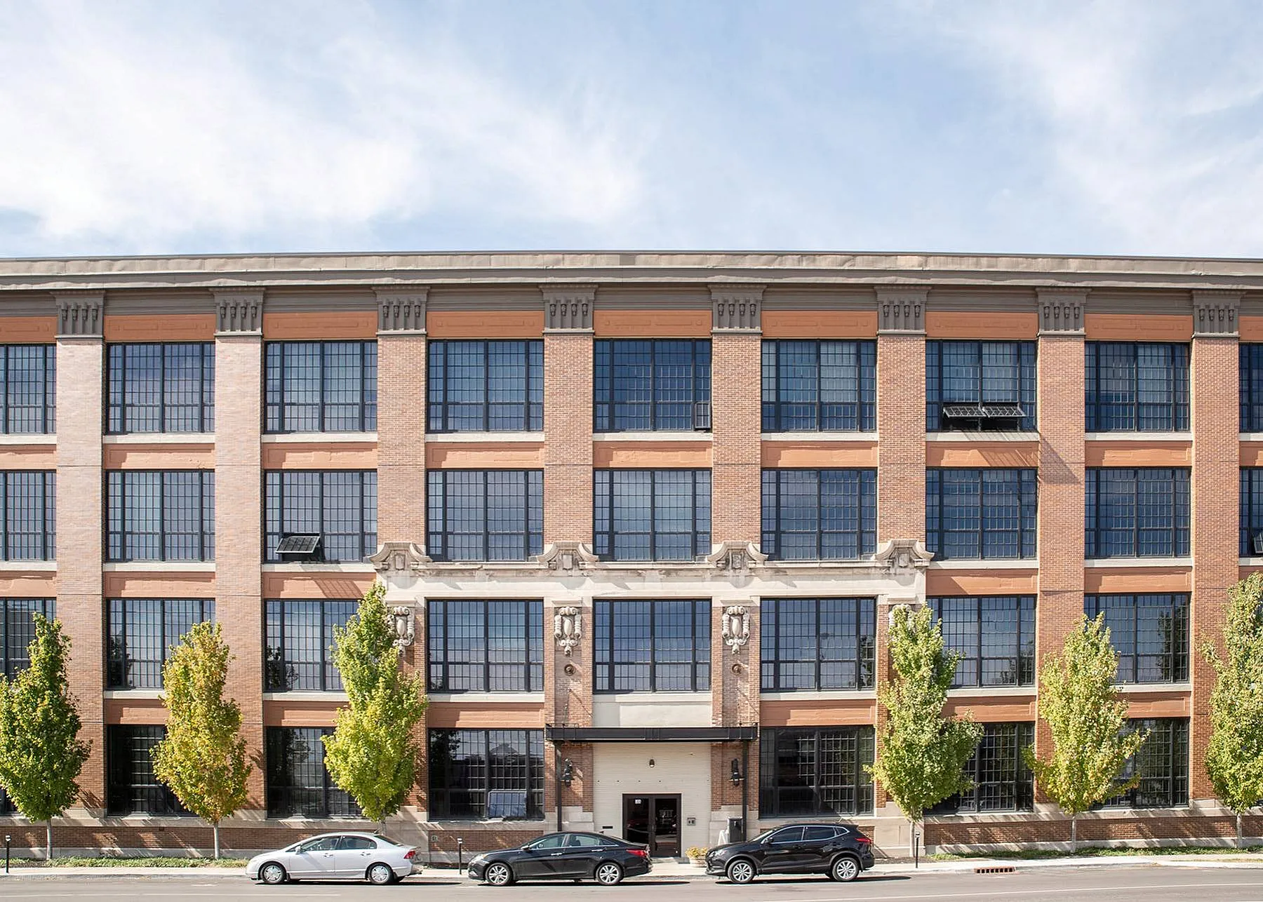 Impressive brick facade of a modern apartment building with large windows and lush green trees lining the street.