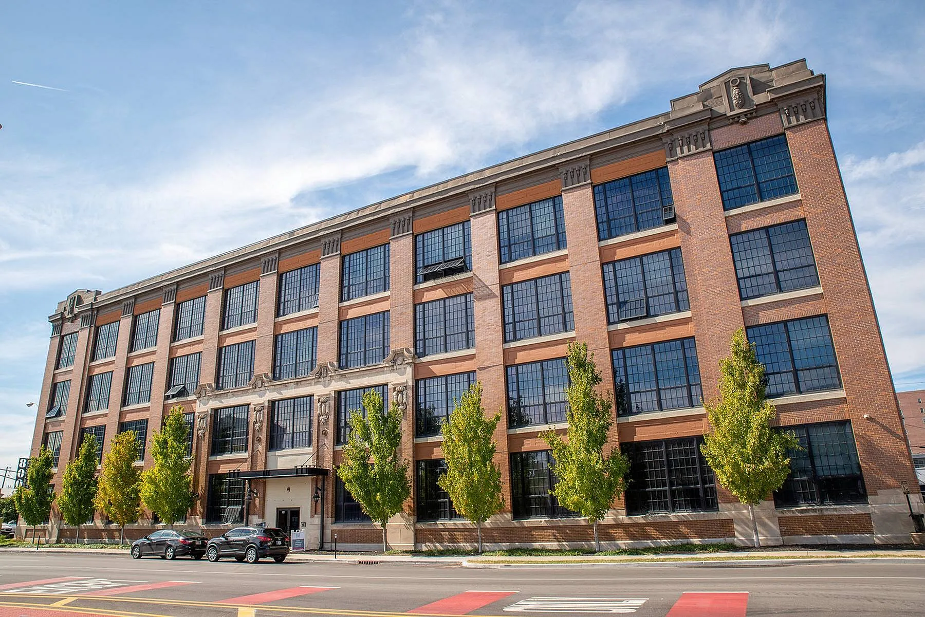 Stunning loft-style apartment building with large industrial windows, framed by lush trees, showcasing its unique architectural charm.
