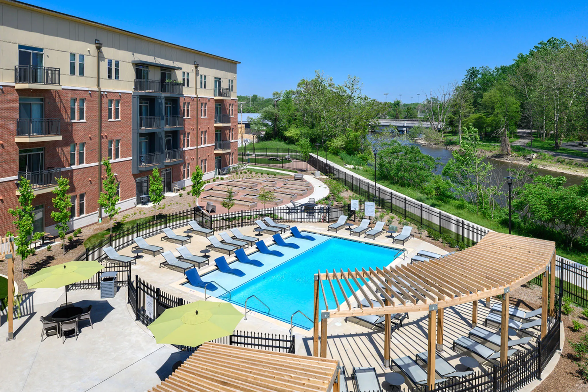 Modern apartment complex with a sparkling outdoor pool, surrounded by sun loungers and lush greenery. Perfect for relaxing and enjoying nature.