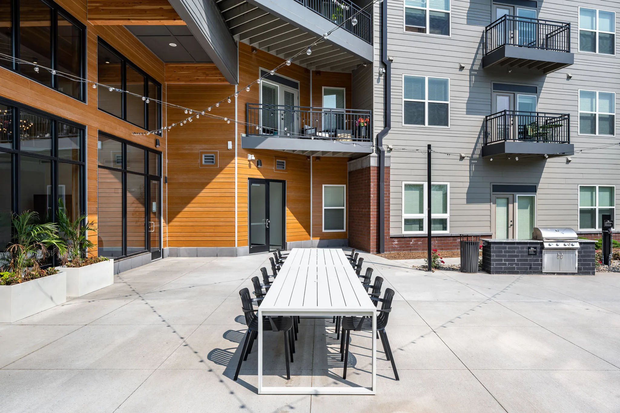 Modern apartment complex courtyard with stylish outdoor dining area, sleek string lighting, and inviting balcony views.