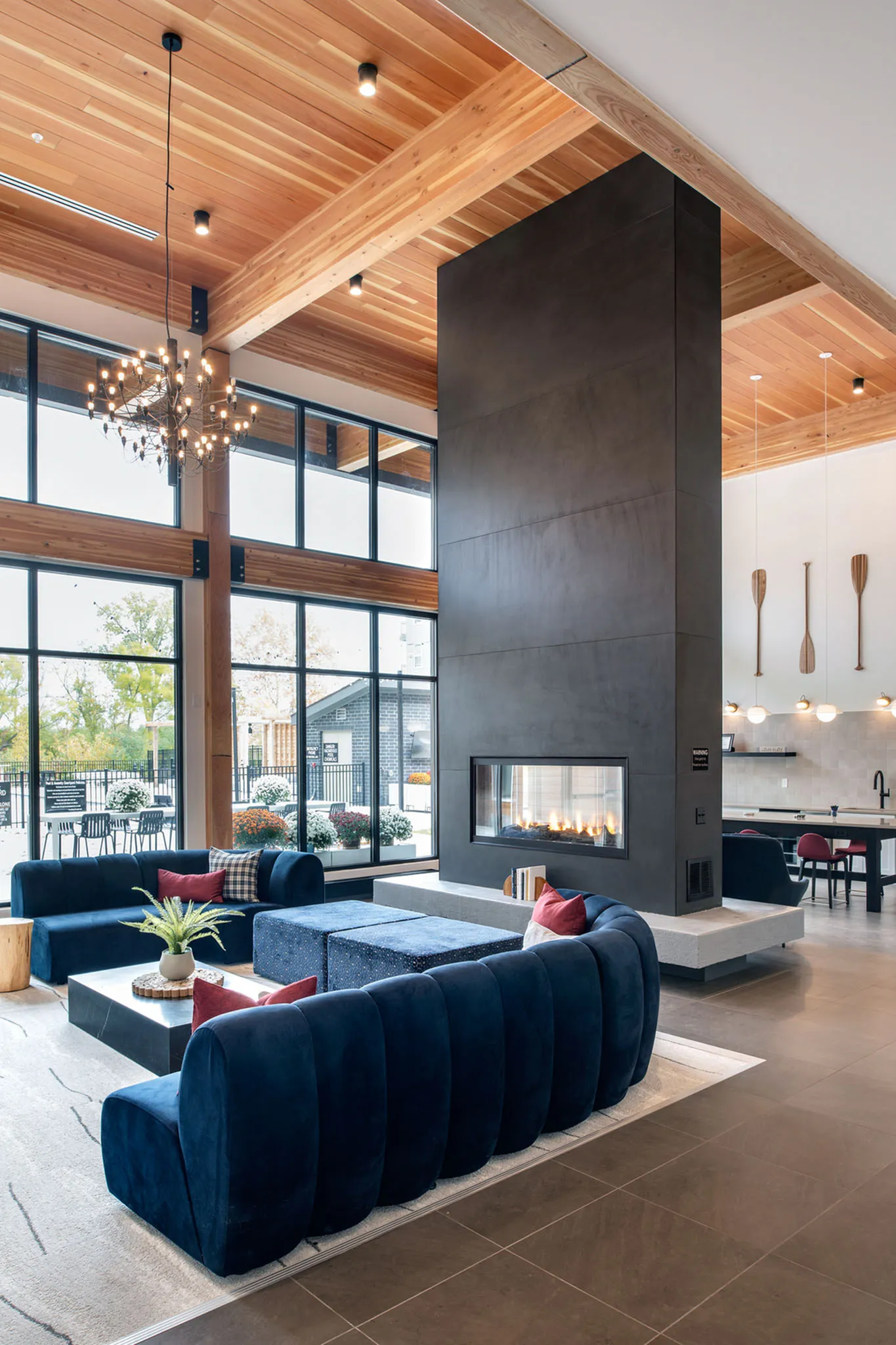 Chic modern living area featuring a cozy fireplace, elegant chandelier, and plush seating against a backdrop of expansive windows and natural light.