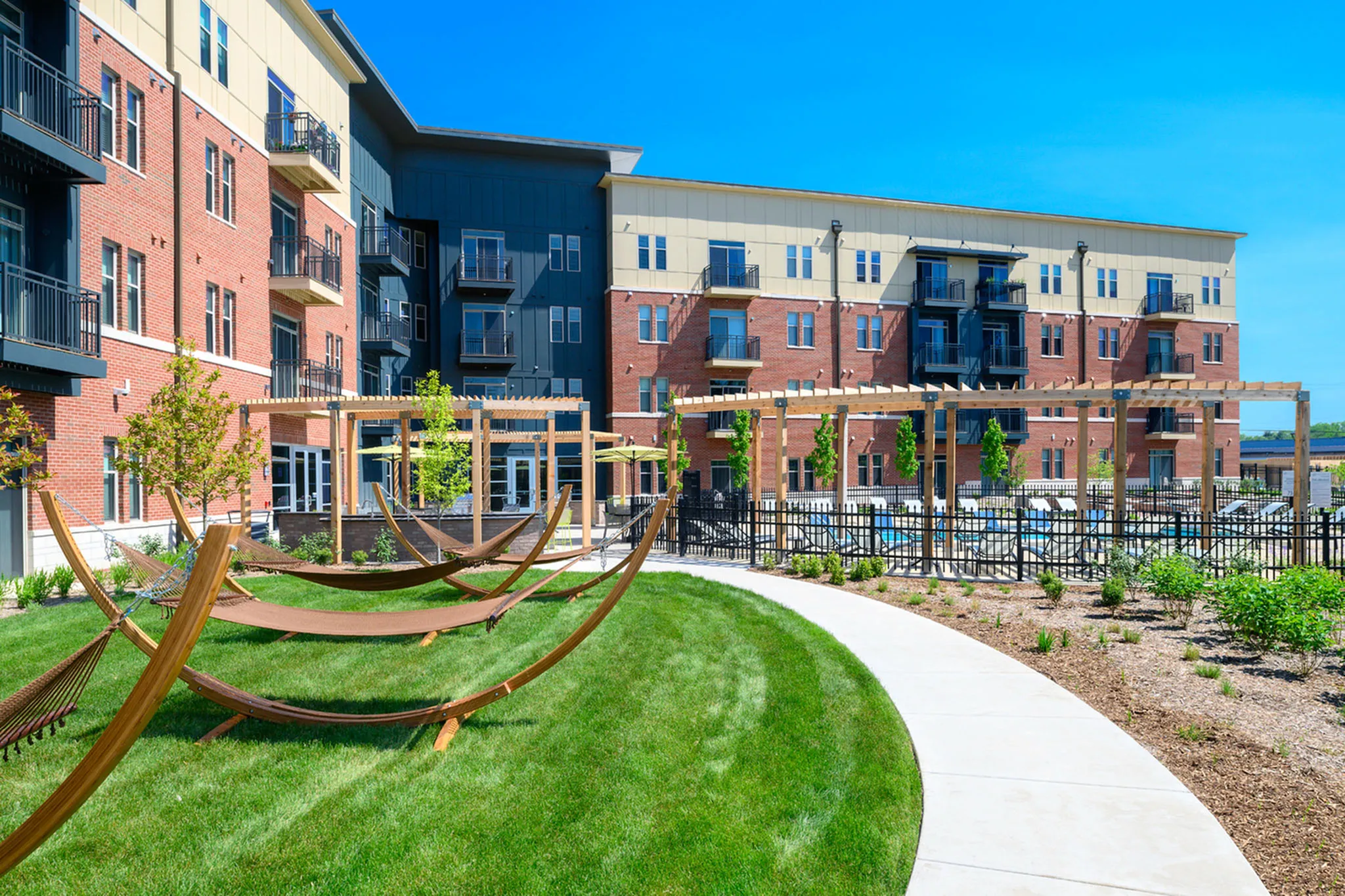 Contemporary apartment complex with a beautifully landscaped courtyard featuring inviting hammocks and pergolas, perfect for relaxation.