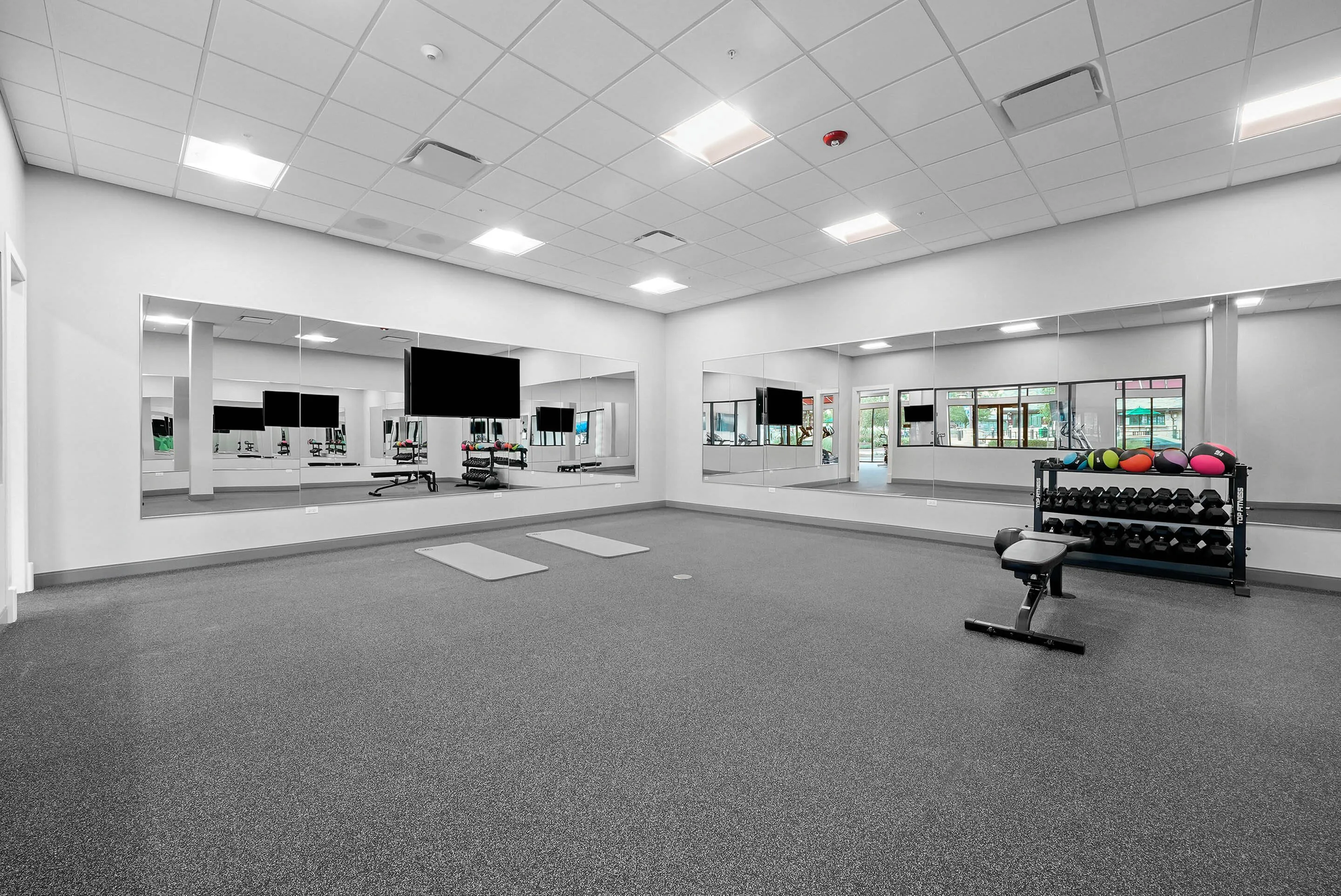 Modern gym with large mirrors, exercise mats, and a vibrant set of weights ideal for fitness enthusiasts.