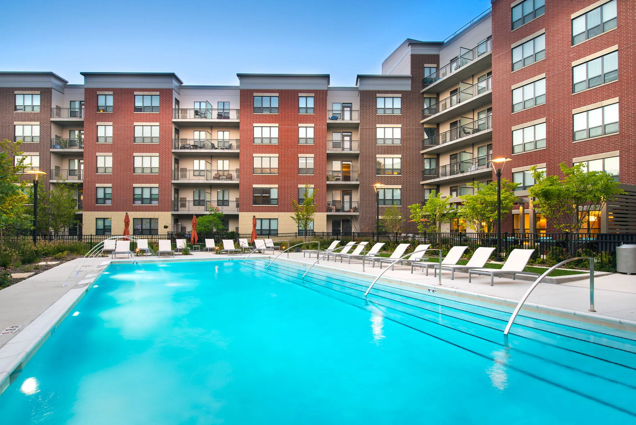 Modern apartment complex with spacious balconies overlooking a pristine outdoor swimming pool and lush landscaping.