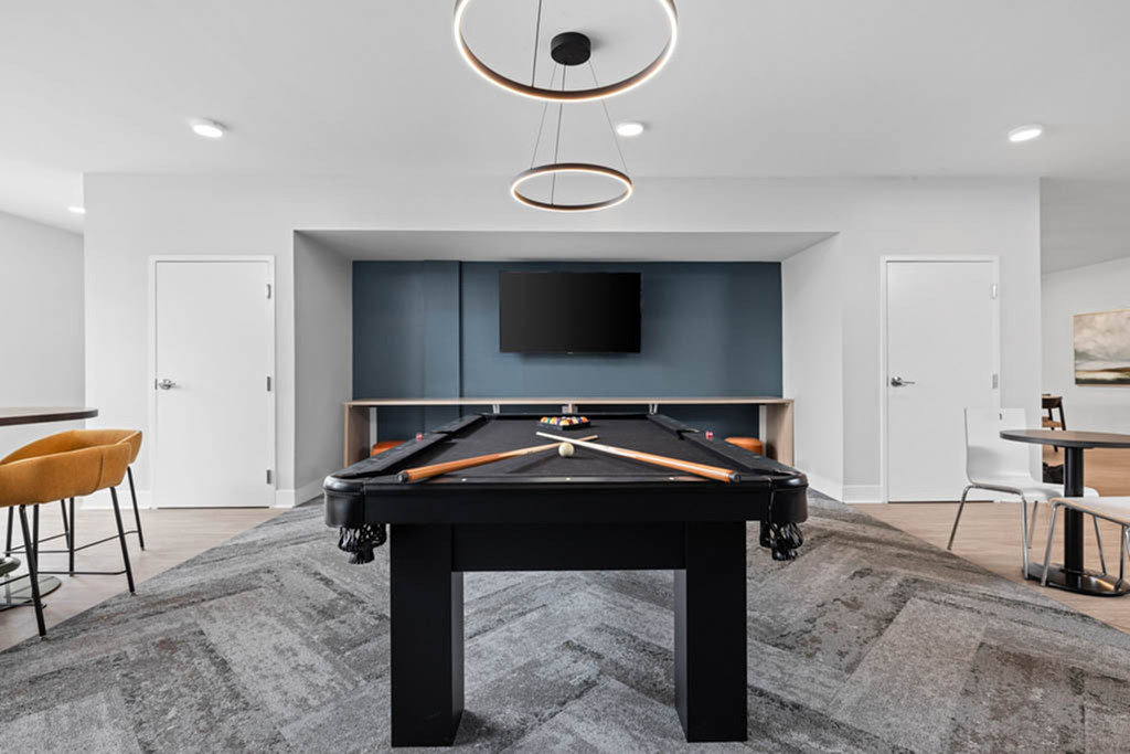 Modern recreation room featuring a sleek black pool table, elegant lighting fixtures, and a wall-mounted TV for entertainment.