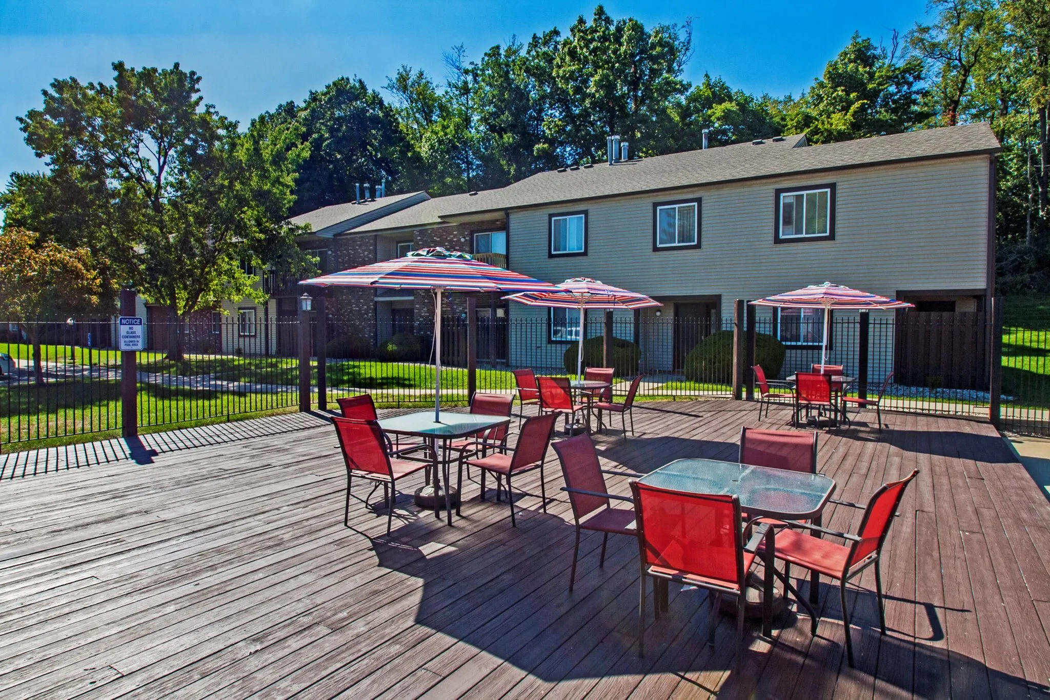 Charming outdoor patio area with vibrant red chairs and striped umbrellas, perfect for relaxation, surrounded by lush greenery and scenic views.