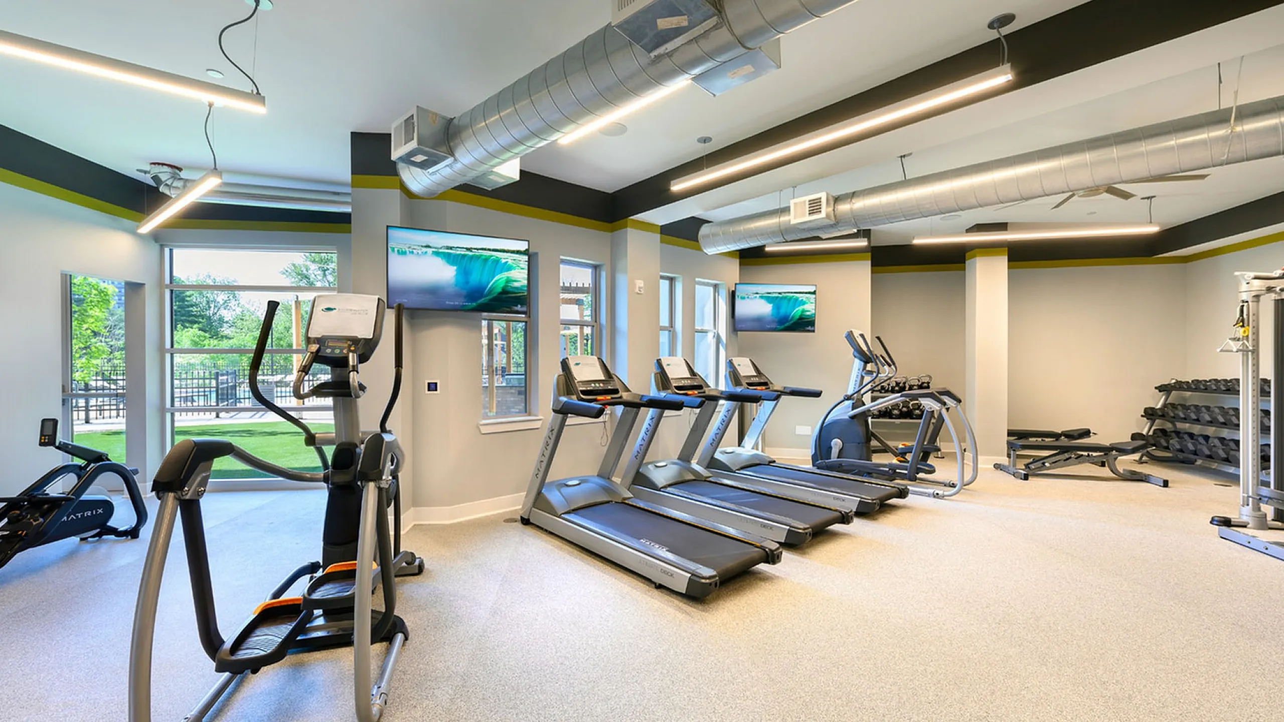Modern fitness center featuring state-of-the-art treadmills, ellipticals, and free weights in a spacious, well-lit environment.