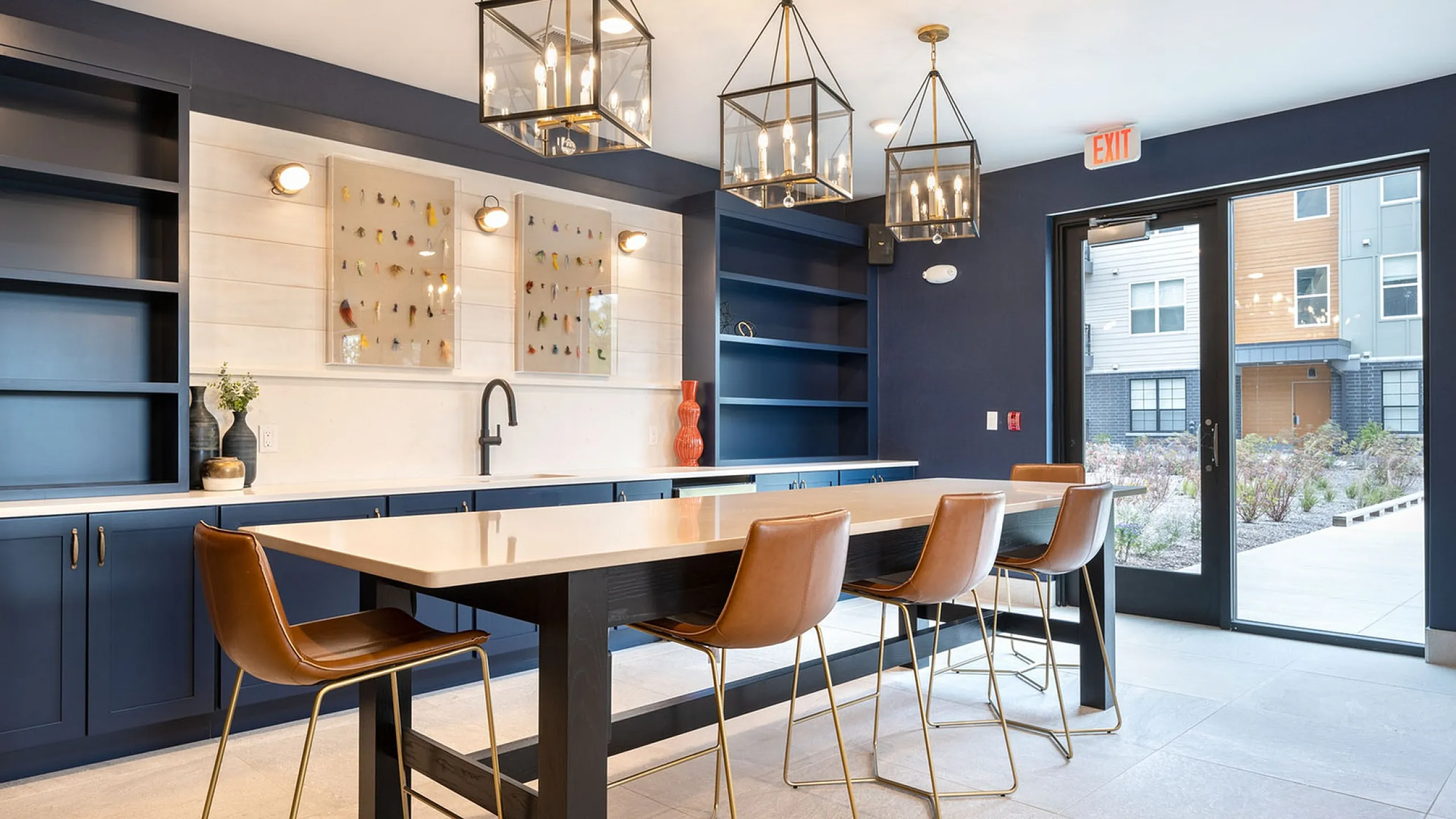 Chic modern kitchen space with elegant lighting fixtures, blue cabinetry, and stylish seating, offering a welcoming ambiance with garden views.