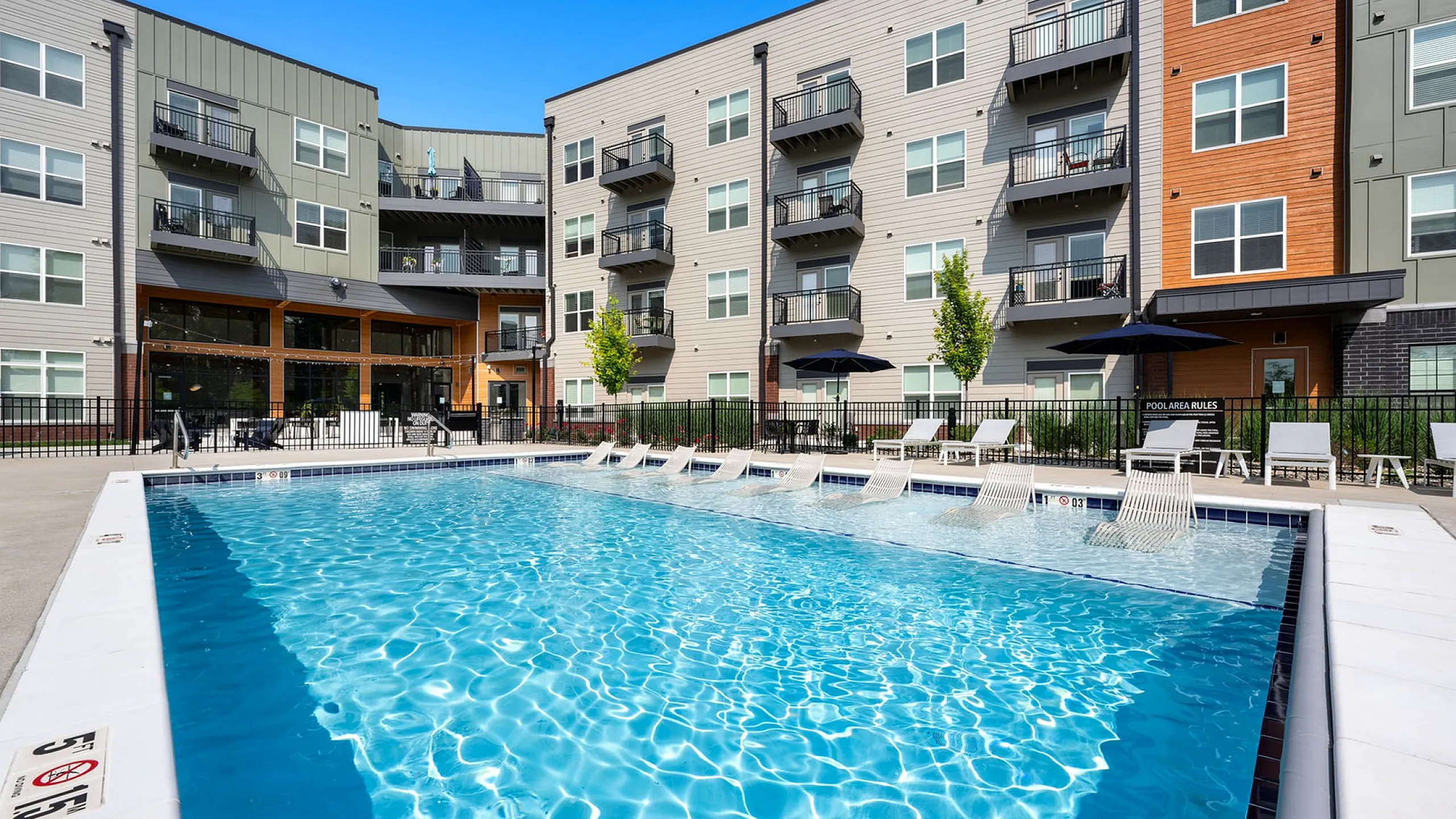 Modern apartment complex with pristine outdoor pool surrounded by lounge chairs, perfect for relaxation.