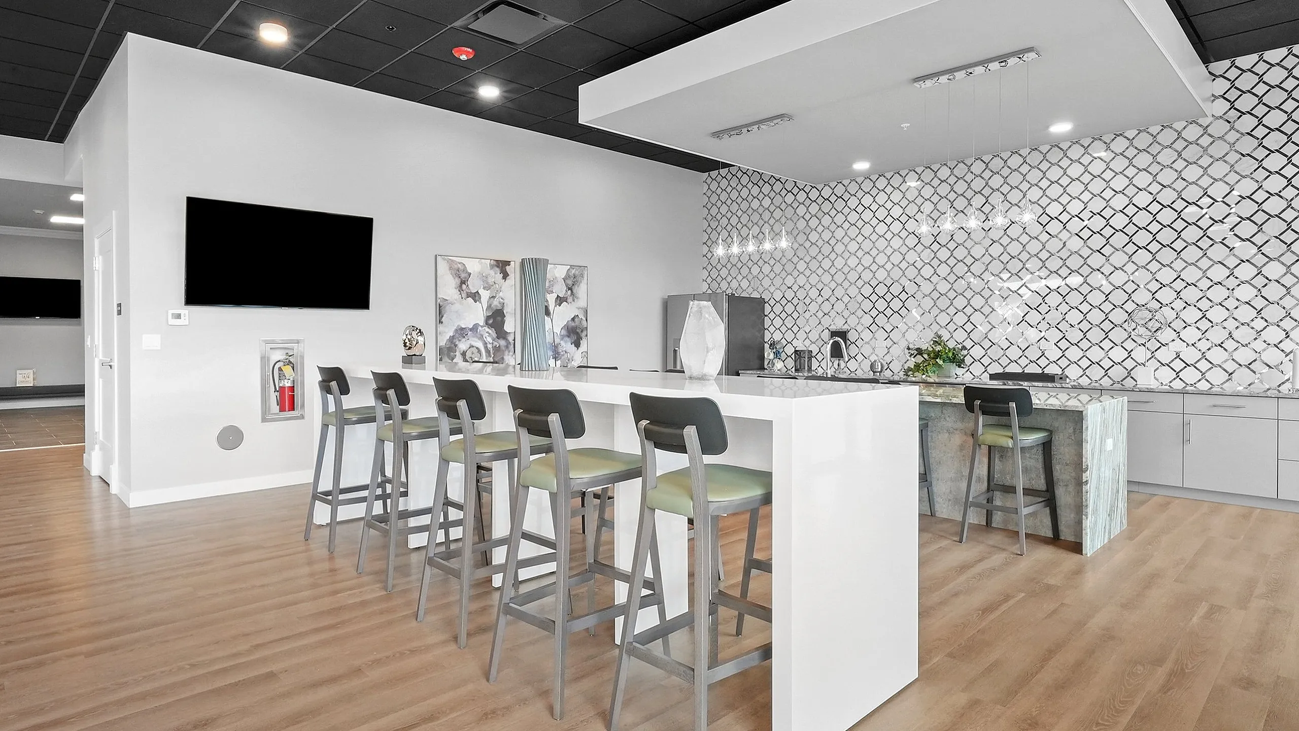 Modern communal kitchen space with sleek bar seating, stylish lighting, and contemporary tile backsplash.