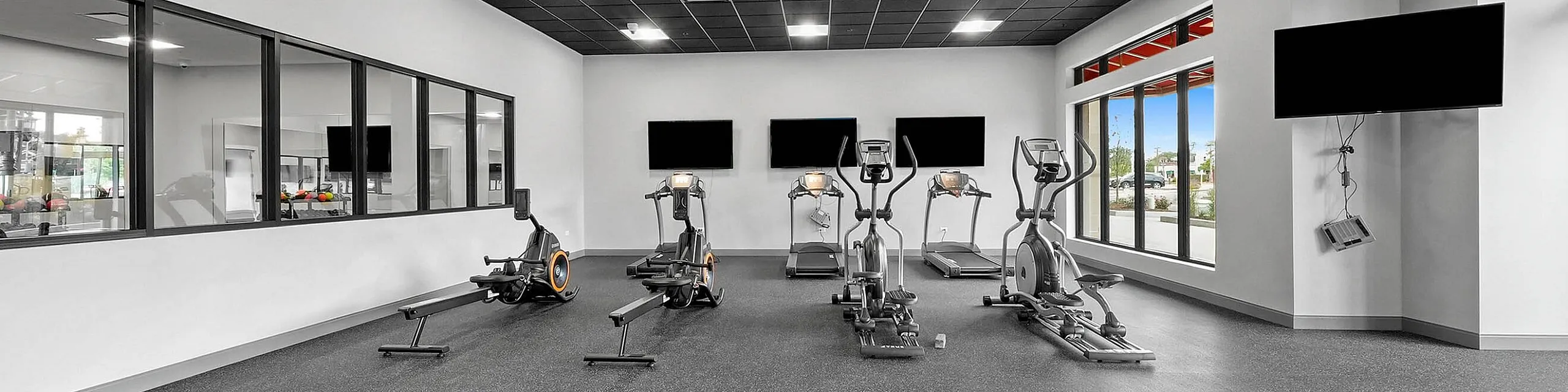 Sleek modern fitness center featuring state-of-the-art exercise equipment, bright windows, and spacious workout area.