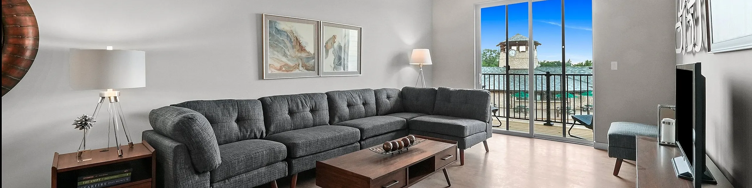 Sophisticated living room with a modern gray sectional sofa, stylish decor, and large glass doors leading to a scenic balcony view.
