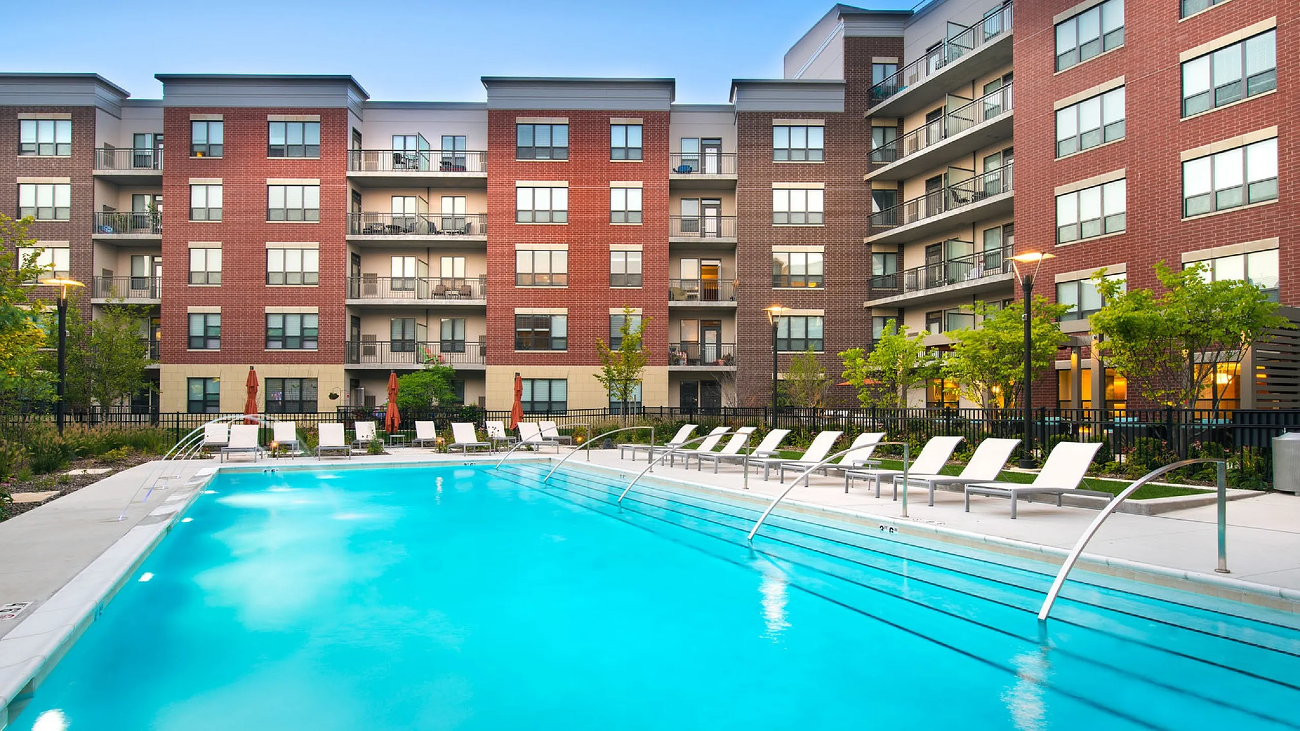 Luxurious apartment complex featuring a pristine outdoor swimming pool, surrounded by modern brick architecture and lush greenery.