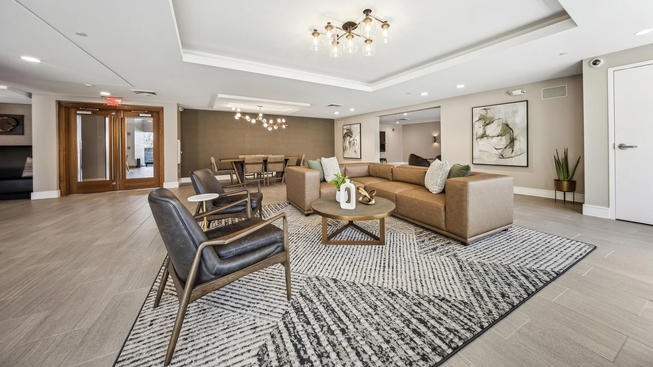 Elegant and spacious lounge featuring sophisticated leather armchairs, a chic sectional sofa, modern light fixtures, and stylish decor on plush rugs.