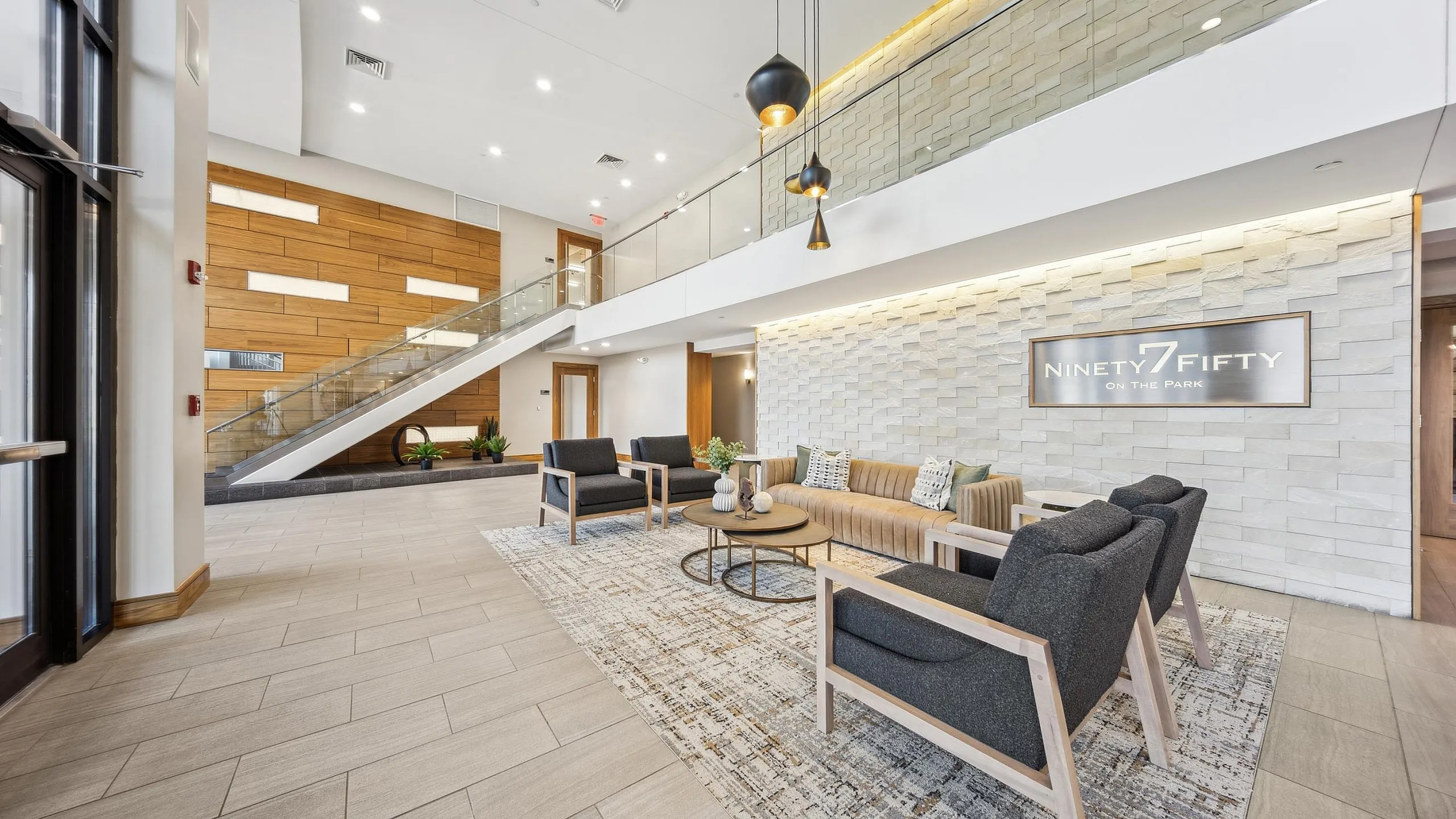 Elegant lobby at Ninety7Fifty on the Park featuring stylish seating, modern lighting, and a chic staircase under a high ceiling.