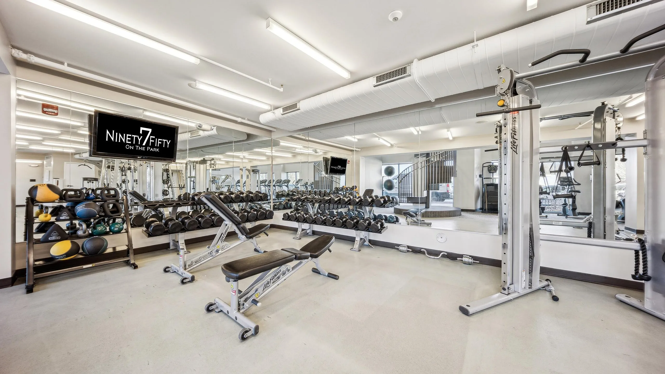 Modern fitness center at Ninety7Fifty on the Park, featuring state-of-the-art equipment, free weights, and a sleek, mirrored interior.