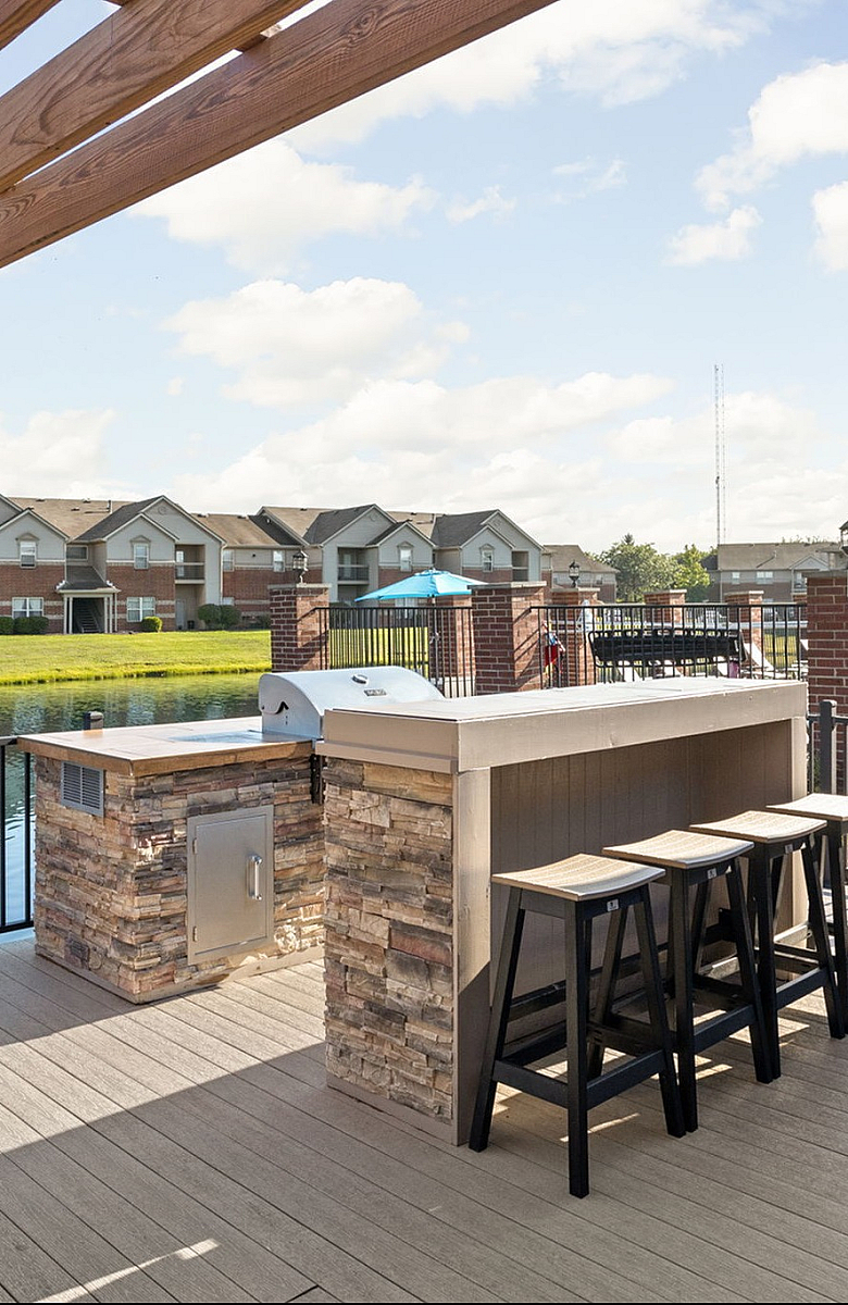 Scenic outdoor patio with a pergola, barbecue area, and seating overlooking a serene lake and community pool.