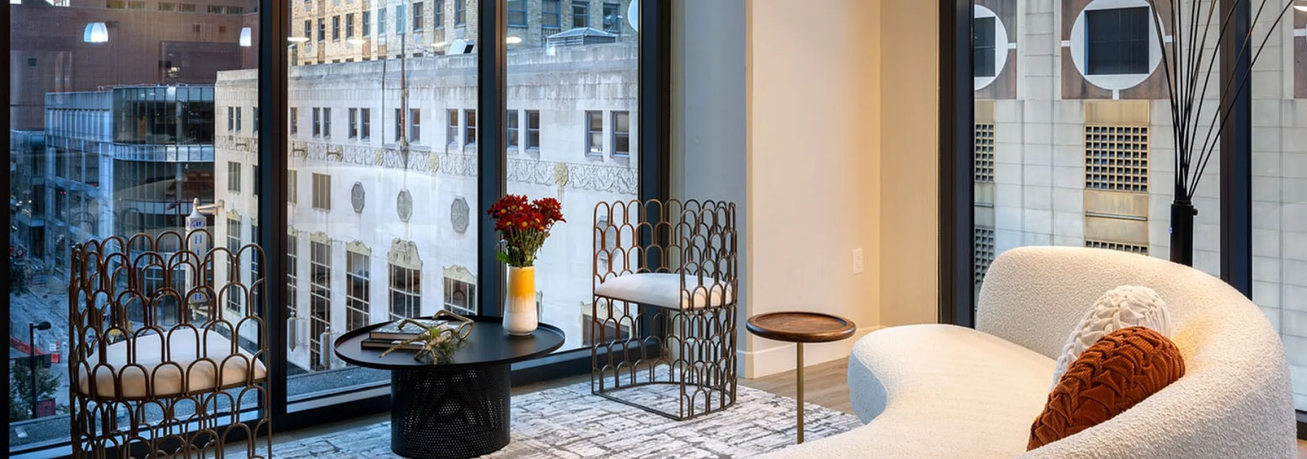 Luxurious apartment lounge with floor-to-ceiling windows, offering stunning city views, modern furniture, and stylish decor.