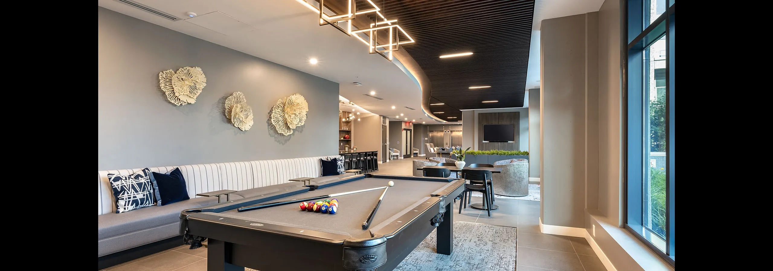 Luxurious communal lounge with modern decor, featuring a sleek billiards table, elegant seating, contemporary art, and ambient lighting.