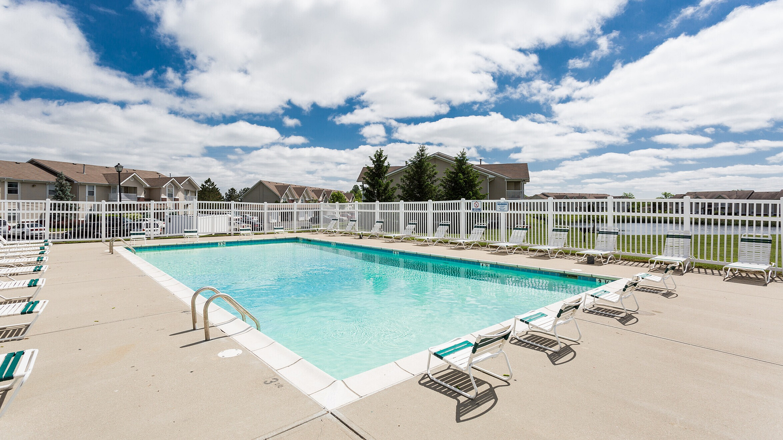 Inviting outdoor swimming pool surrounded by lounge chairs, nestled in a serene residential area with bright blue skies overhead.