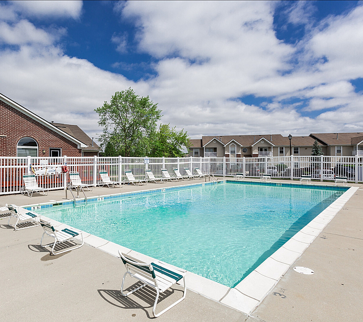 Inviting outdoor pool area with lounge chairs, surrounded by a white picket fence and charming brick architecture under a bright blue sky.
