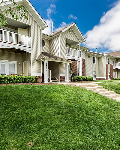 Inviting apartment complex with charming balconies, lush green lawns, and a bright, welcoming exterior under a clear blue sky.