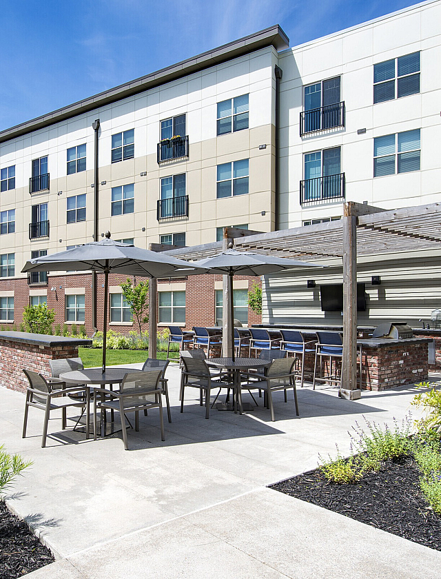 Modern apartment complex with stylish outdoor seating area and lush landscaping under a clear blue sky.