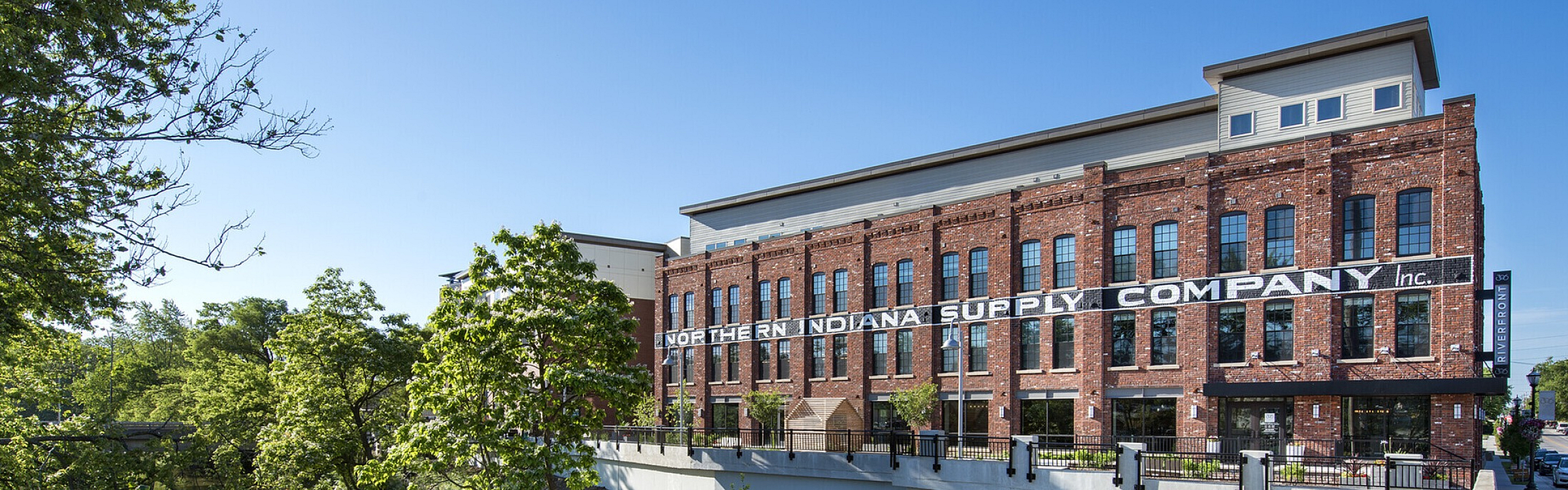 Charming riverside building with classic red brick facade, surrounded by lush greenery and a serene water view.