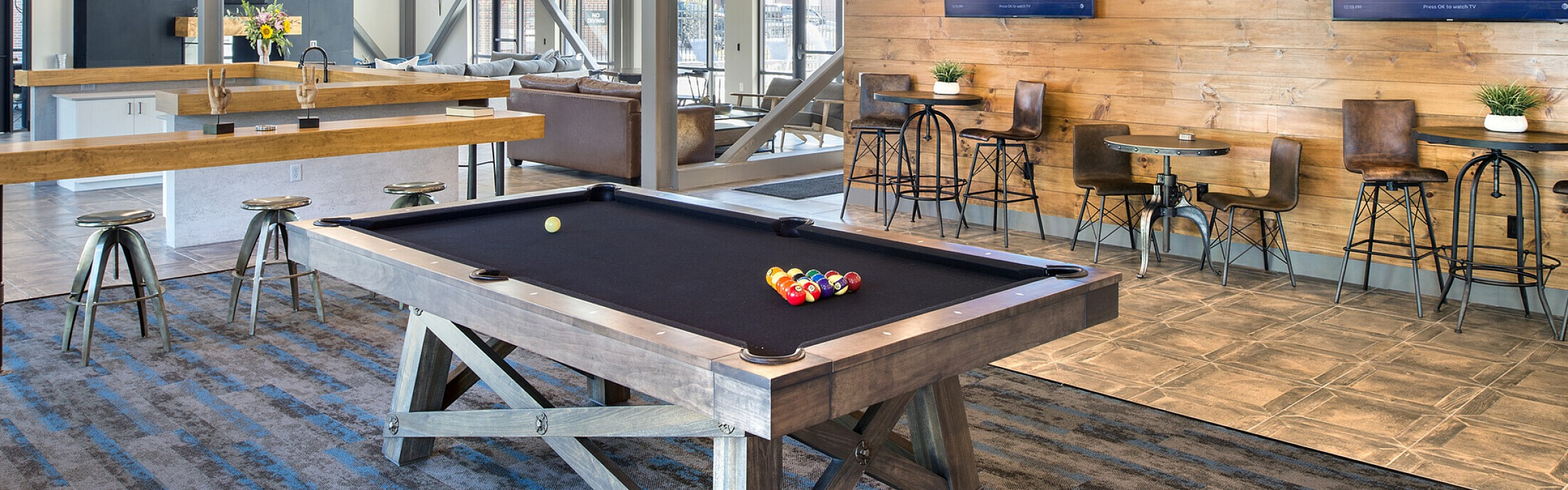 Chic game room with a stylish pool table, modern bar seating, and wall-mounted TVs for an upscale entertaining experience.
