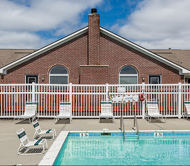 Inviting brick apartment with charming arched windows, complemented by a refreshing pool and sunlit loungers, offering perfect relaxation.