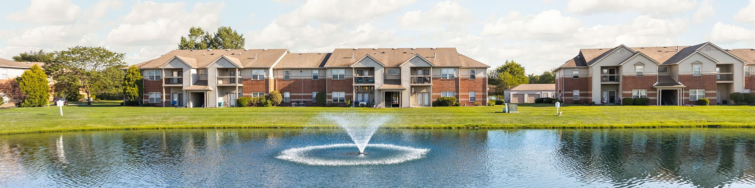 Charming apartment complex with picturesque lakeside views and tranquil fountain, nestled in a serene natural setting.
