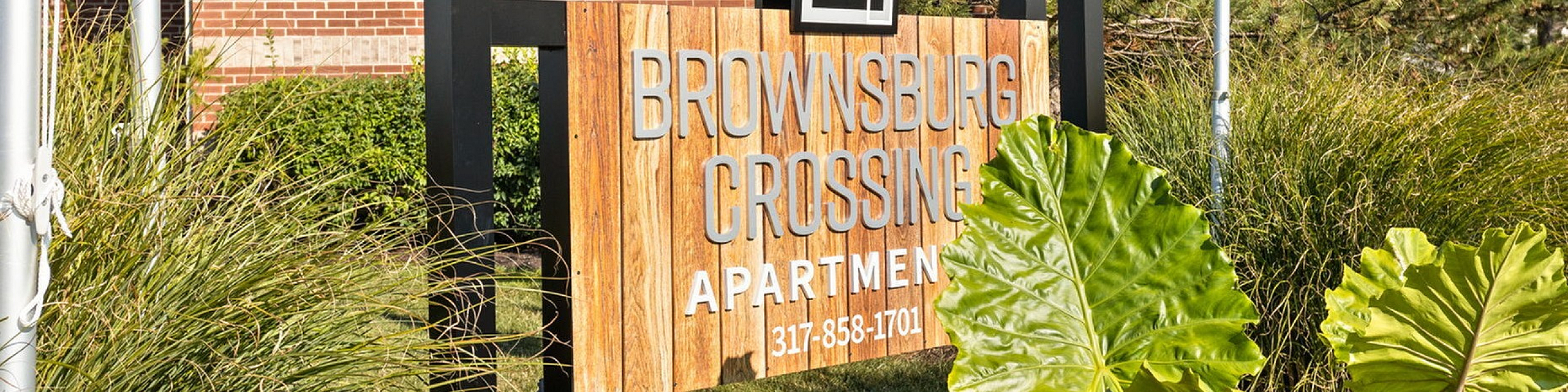 Inviting Brownsburg Crossing Apartments entrance sign surrounded by lush greenery and bright red flowers.
