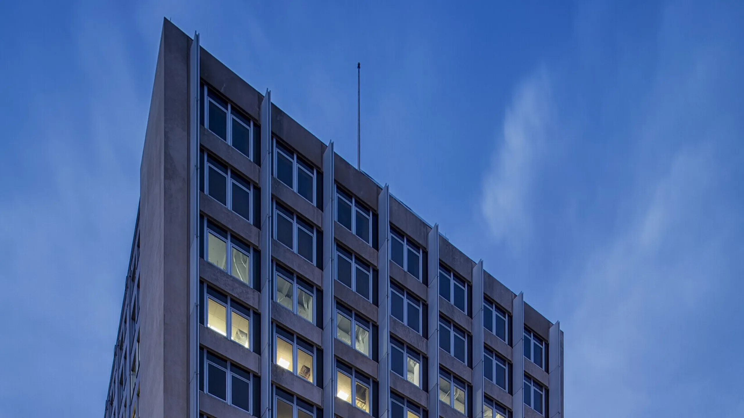 Modern high-rise apartment building illuminated during twilight, showcasing an urban lifestyle with convenient amenities.