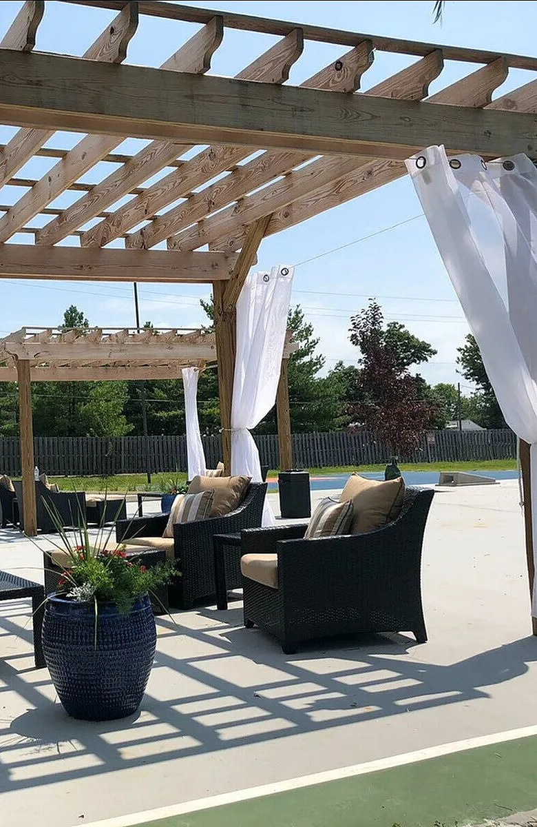 Chic outdoor patio with a wooden pergola, flowing white curtains, elegant seating, and lush greenery for a serene retreat.