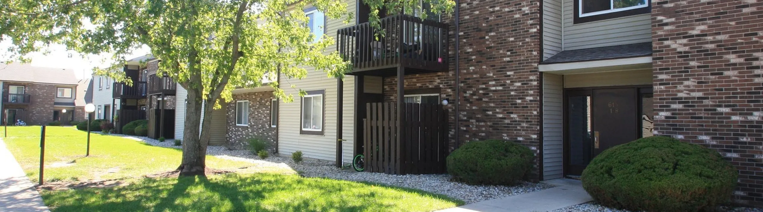 Charming apartment complex with brick facade and lush greenery, highlighting a serene and welcoming environment.