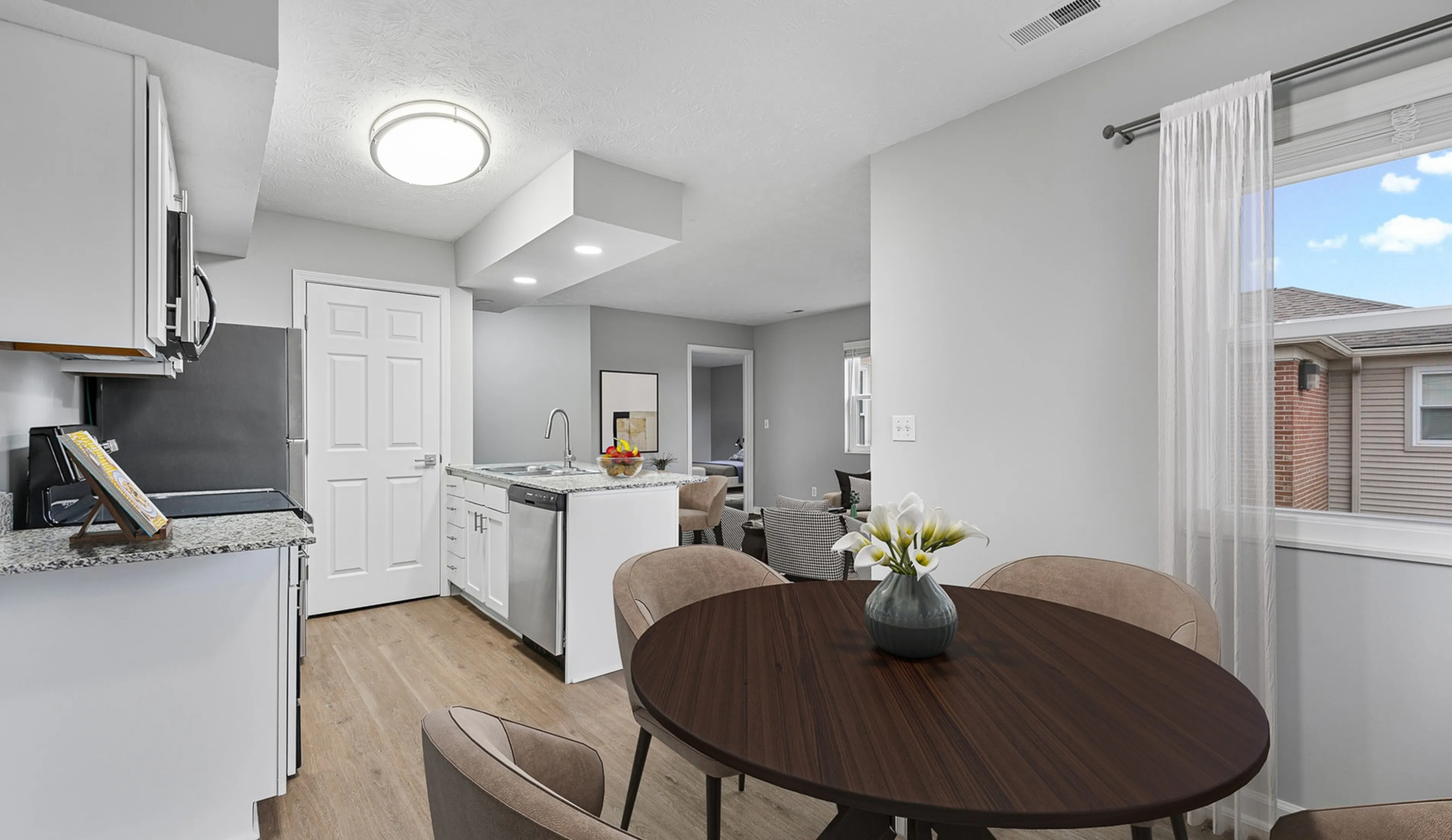 Modern kitchen with sleek cabinetry, granite countertops, and open layout flowing into a bright dining area with a large window.